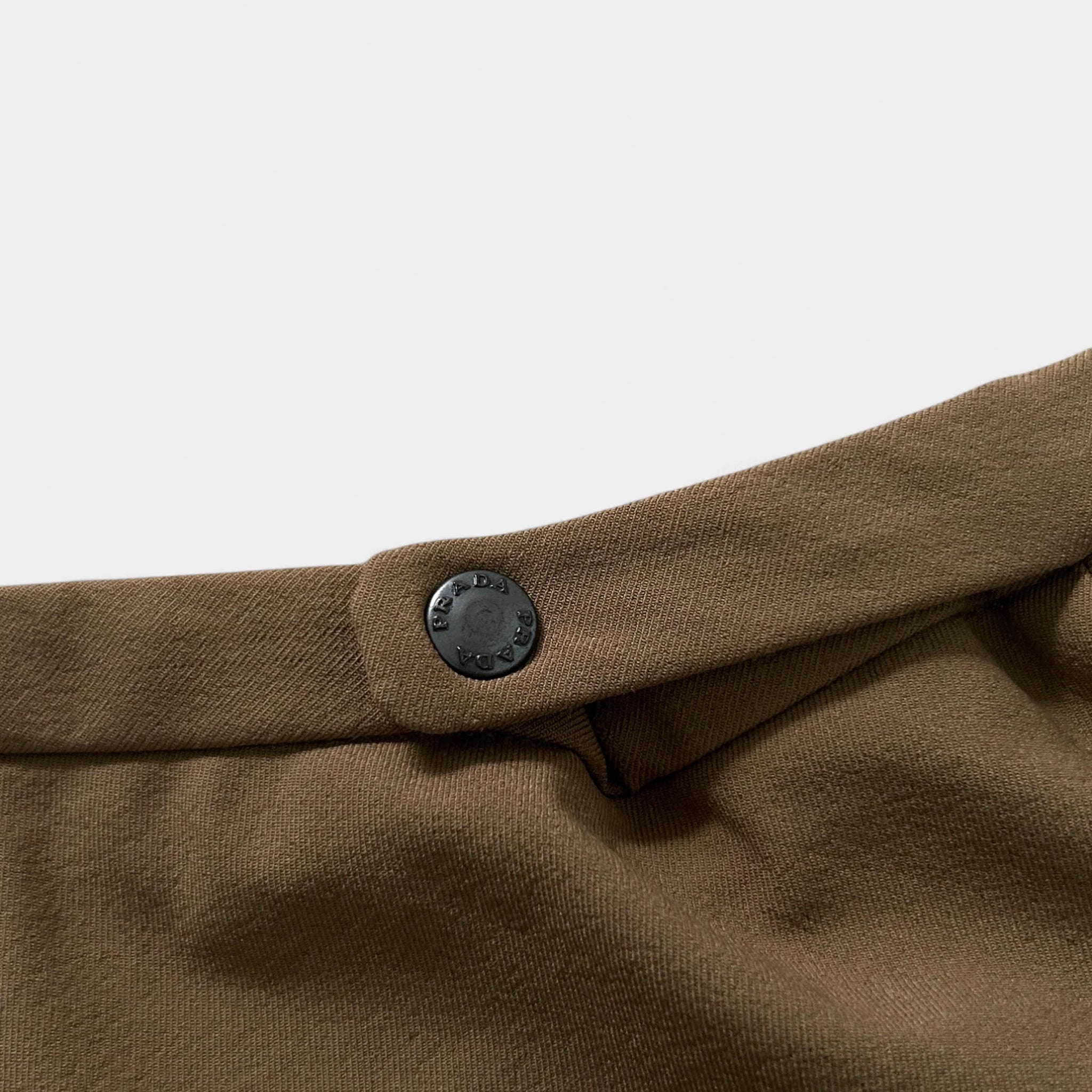 A close-up view of a brown fabric, possibly a skirt or blouse, with a black button visible on the waistband.