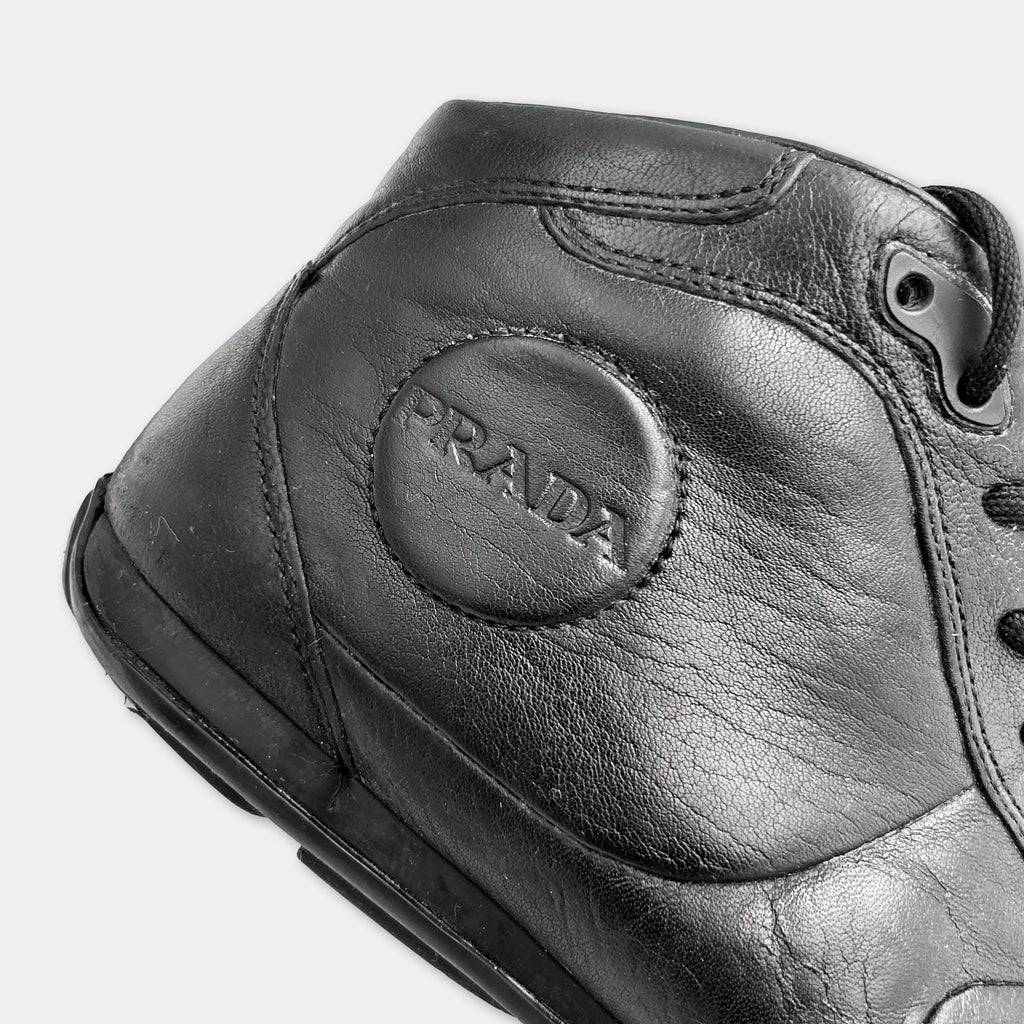 A close-up view of a black leather shoe with the brand name "PRADA" embossed on the side.