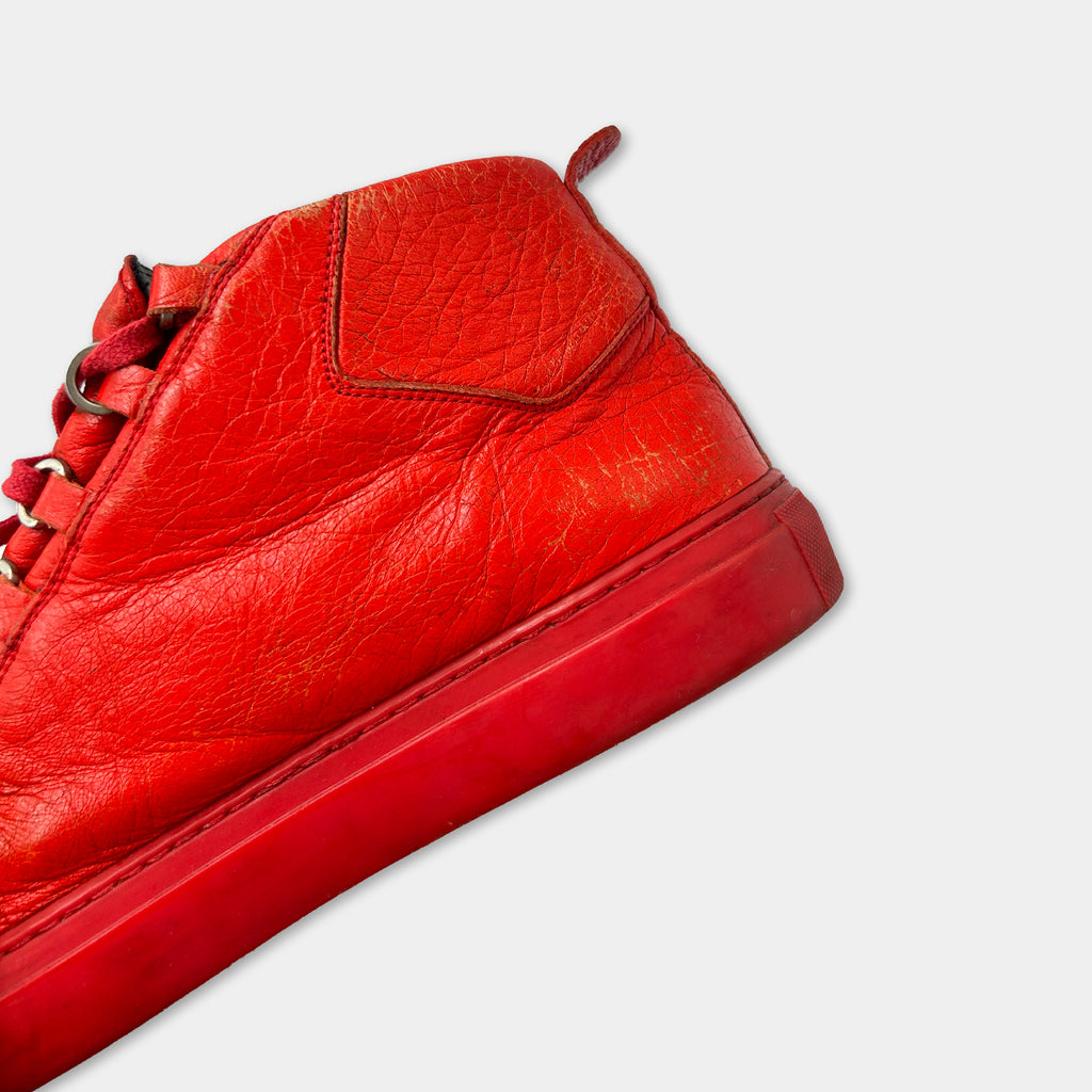 A close-up view of a bright red high-top sneaker with a red sole and laces.