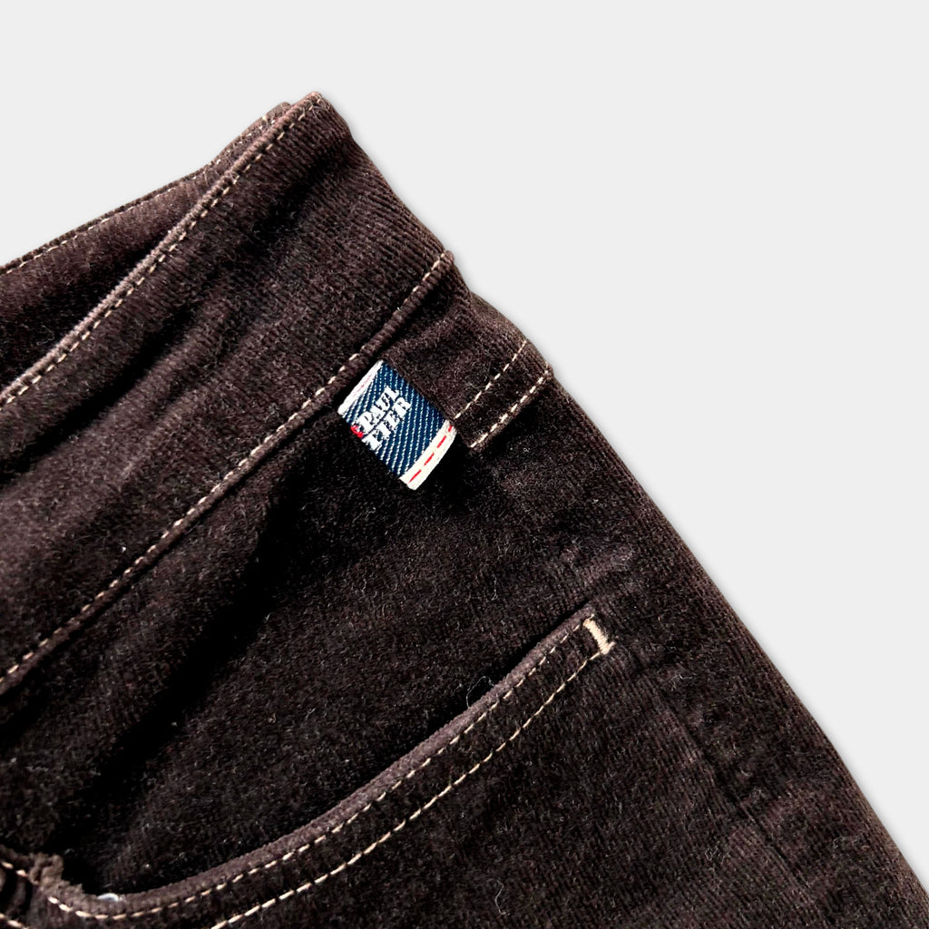 A close-up view of a dark brown pair of jeans, with a small label or tag attached to the pocket.