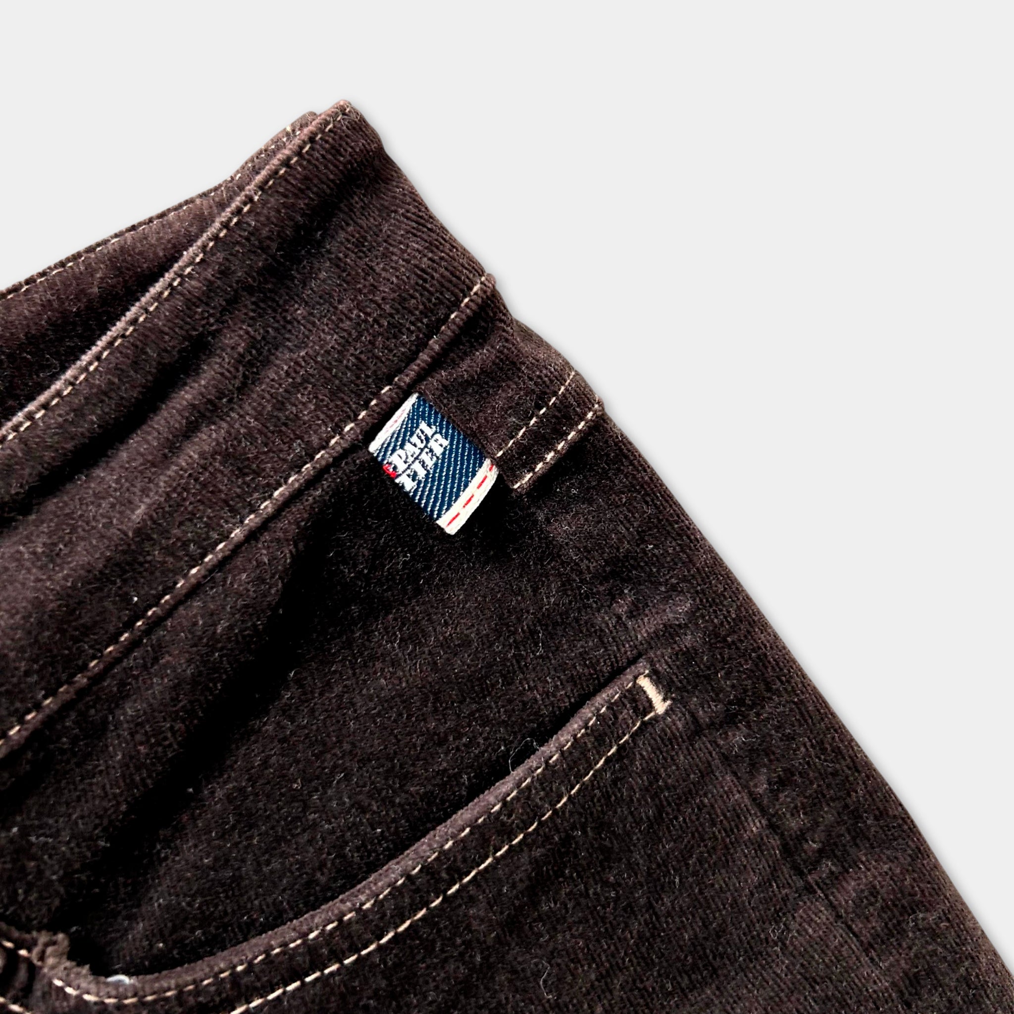 A close-up view of a dark brown pair of jeans, with a small label or tag attached to the pocket.
