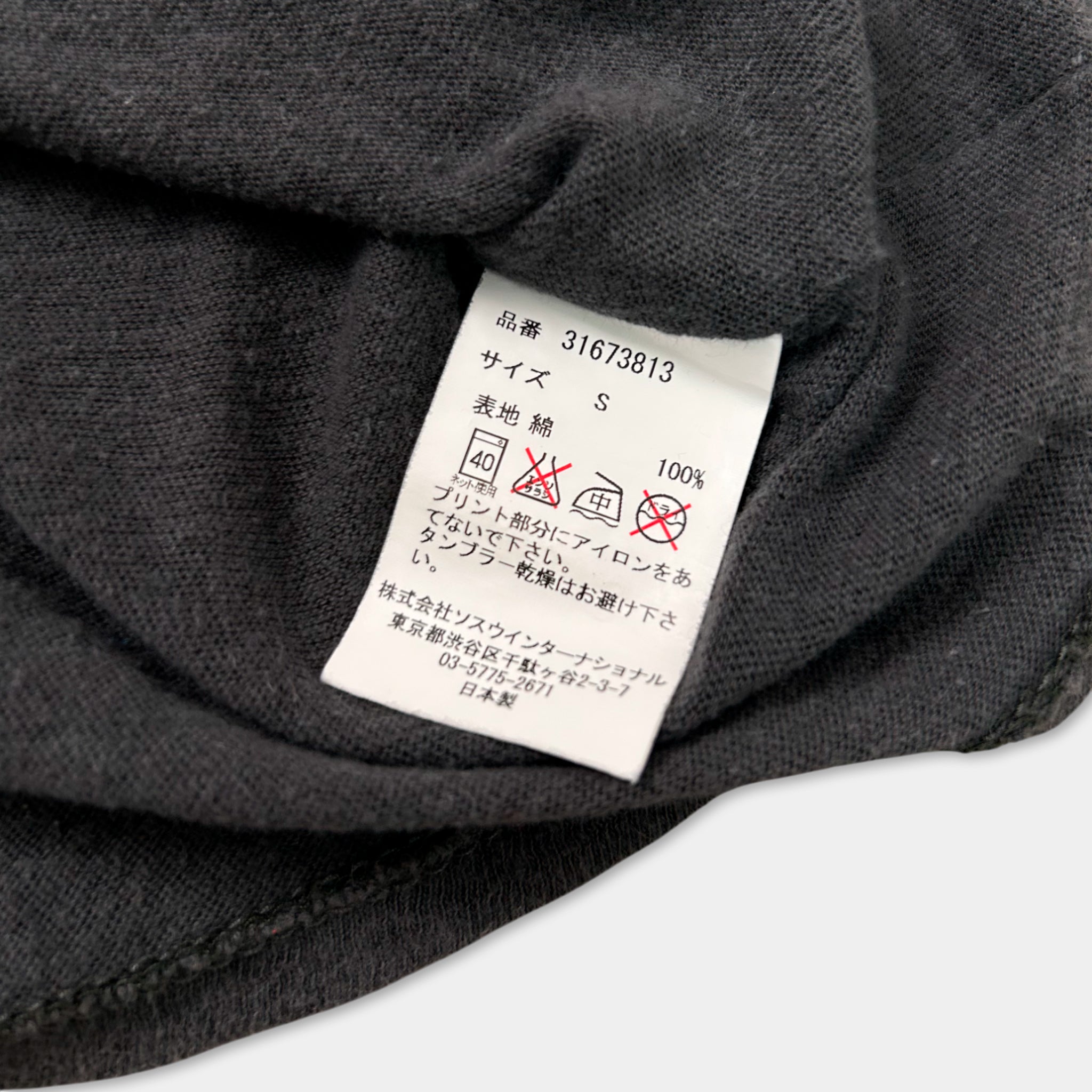 a close-up view of a black fabric, possibly a sweater or garment, with a white label attached to it. The label contains text in Japanese and English, along with some symbols and numbers, likely indicating the garment's size, care instructions, or other relevant information.