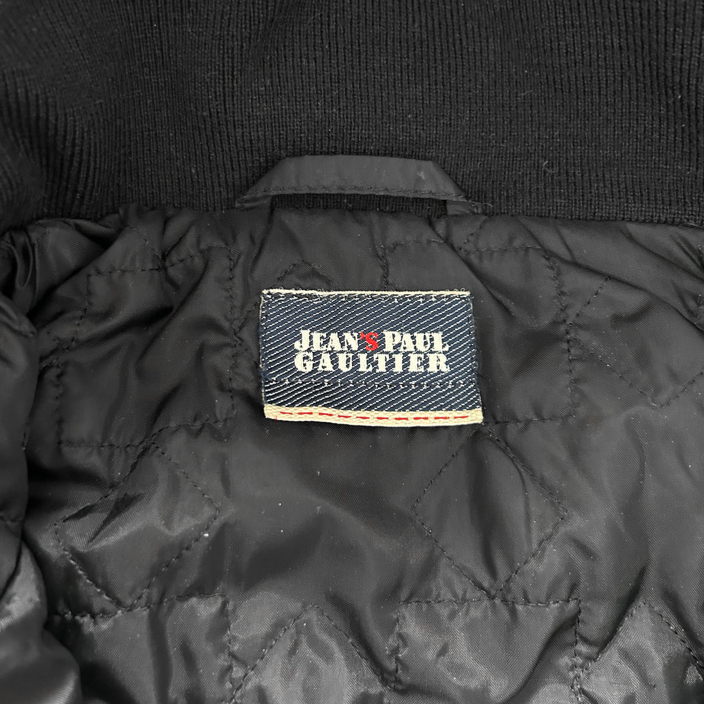 a close-up view of a black jacket with a label on the back, displaying the brand name "Jean Paul Gaultier".