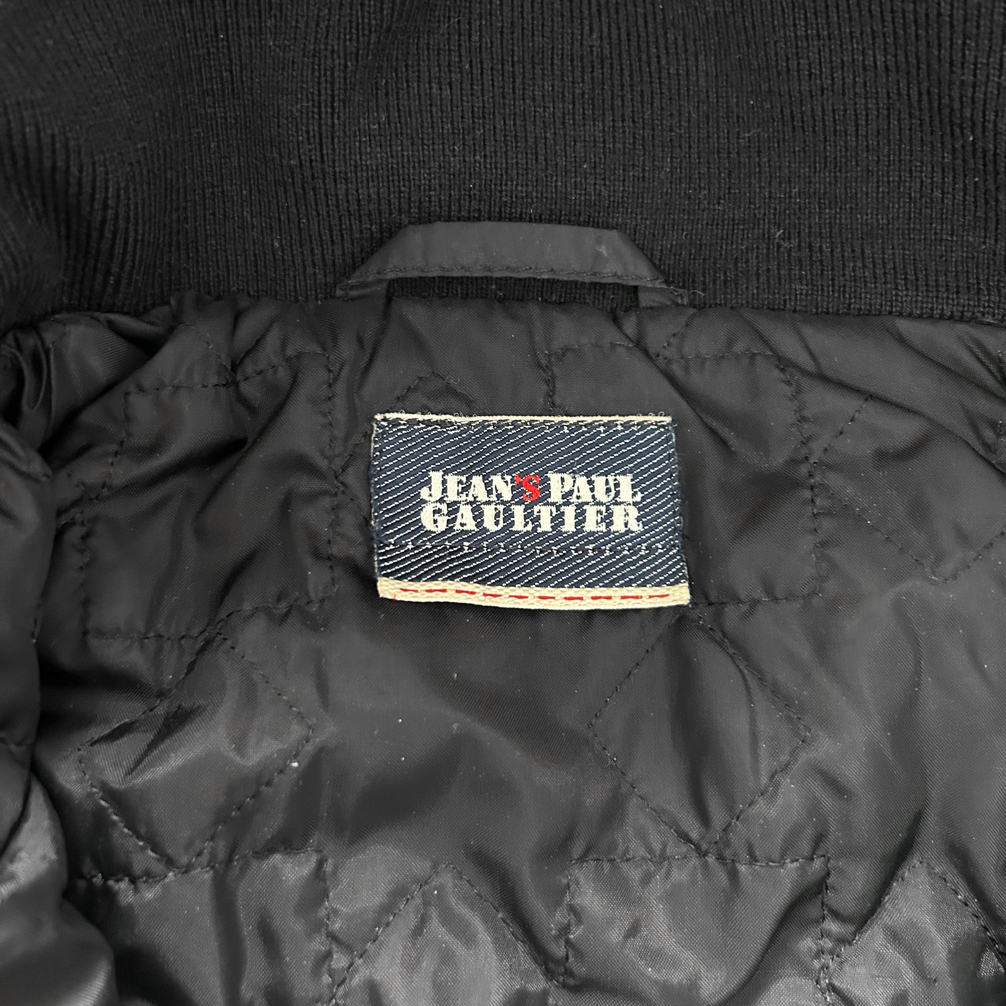 a close-up view of a black jacket with a label on the back, displaying the brand name "Jean Paul Gaultier".