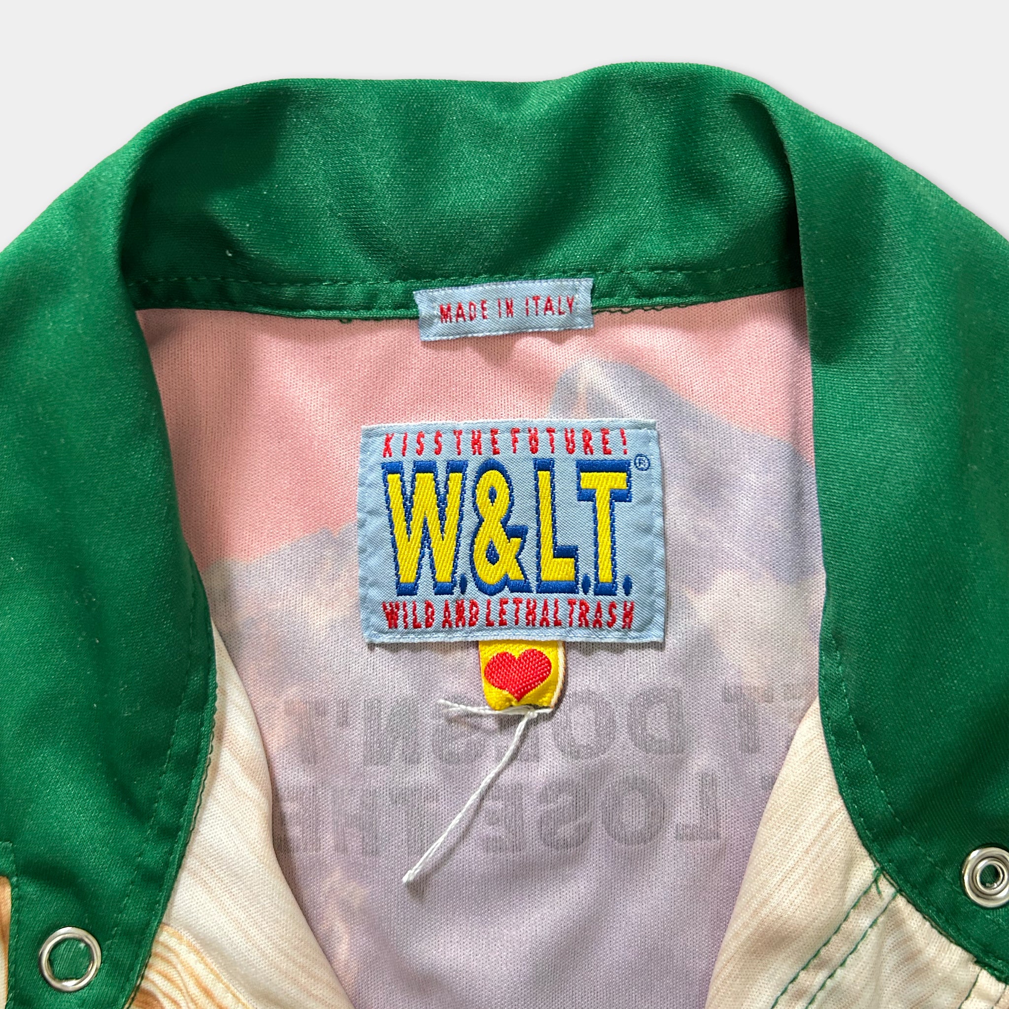 a close-up view of a green and white jacket with a label on the collar, which reads "Made in Italy" and features the W&L logo and the text "Kissing the future! W&L wild and illegal trash".
