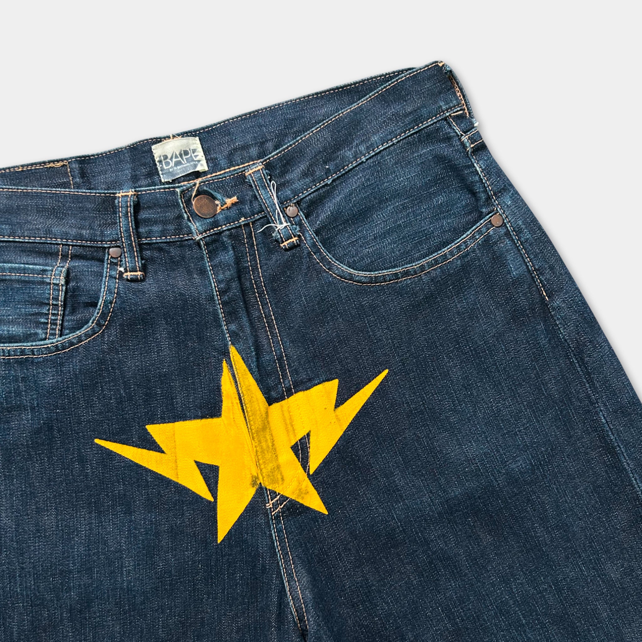 A pair of blue jeans with a yellow lightning bolt design on the front pocket area.