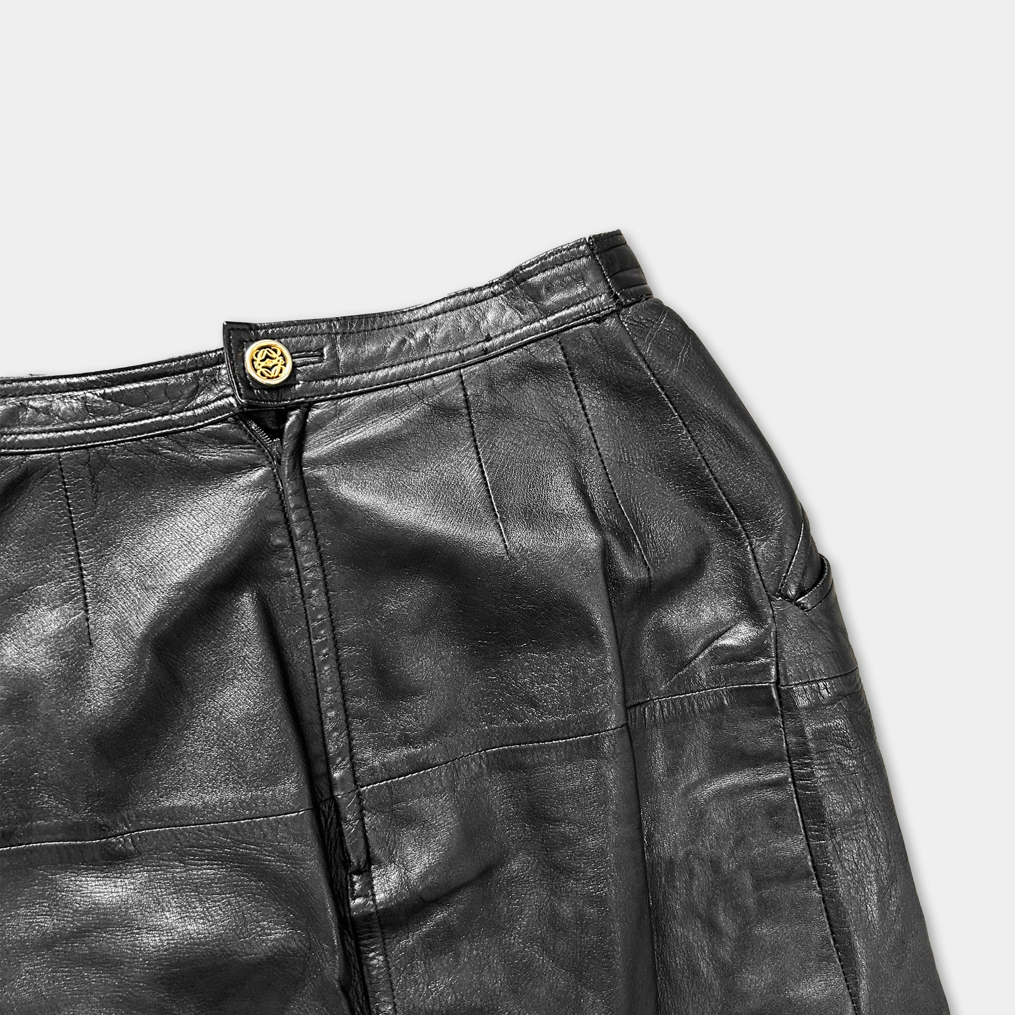A close-up view of a pair of black leather pants with a gold button on the waistband.