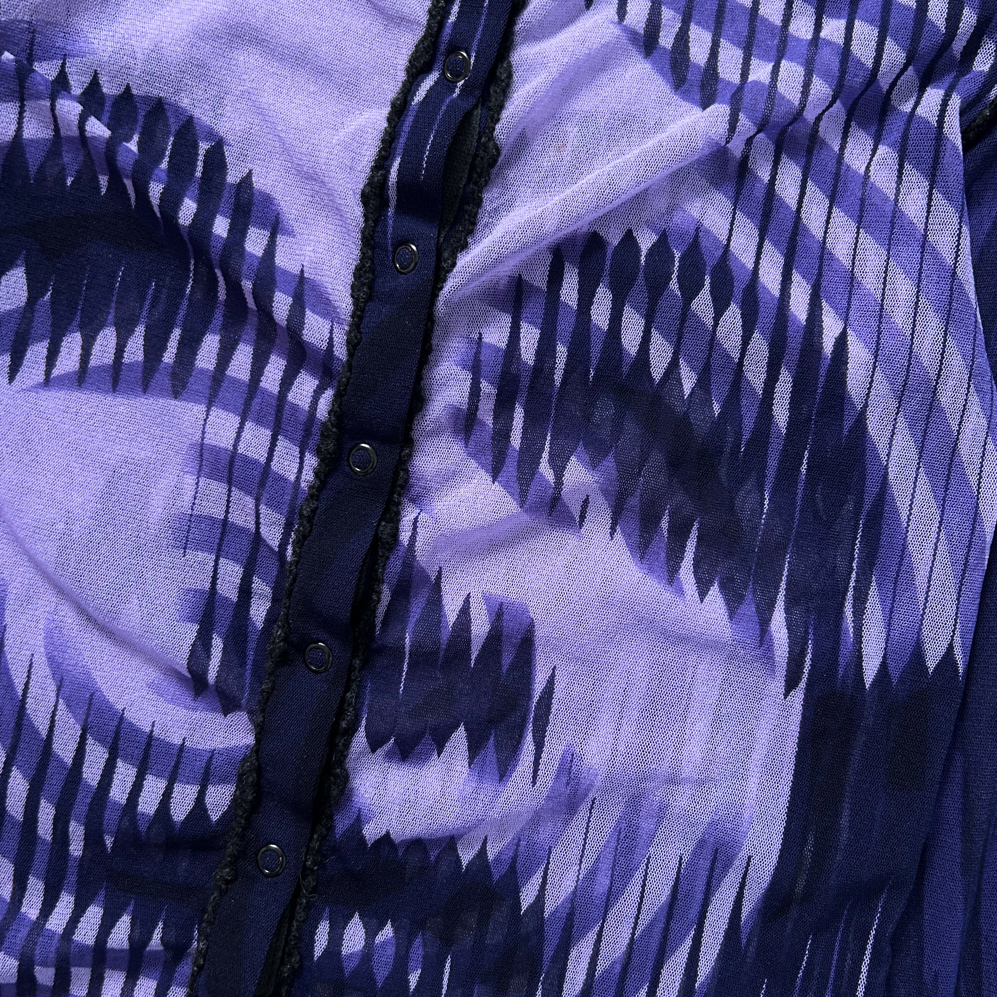 a close-up view of a fabric with a purple and black pattern, featuring a button and a ruffled edge.