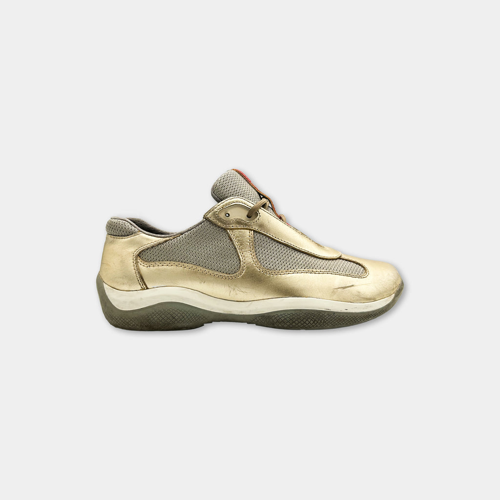 A single, gold-colored sneaker with a mesh upper and a white sole, positioned against a plain white background.