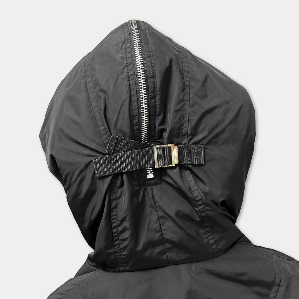 A close-up view of the back of a black hooded jacket with a zipper and a black strap.