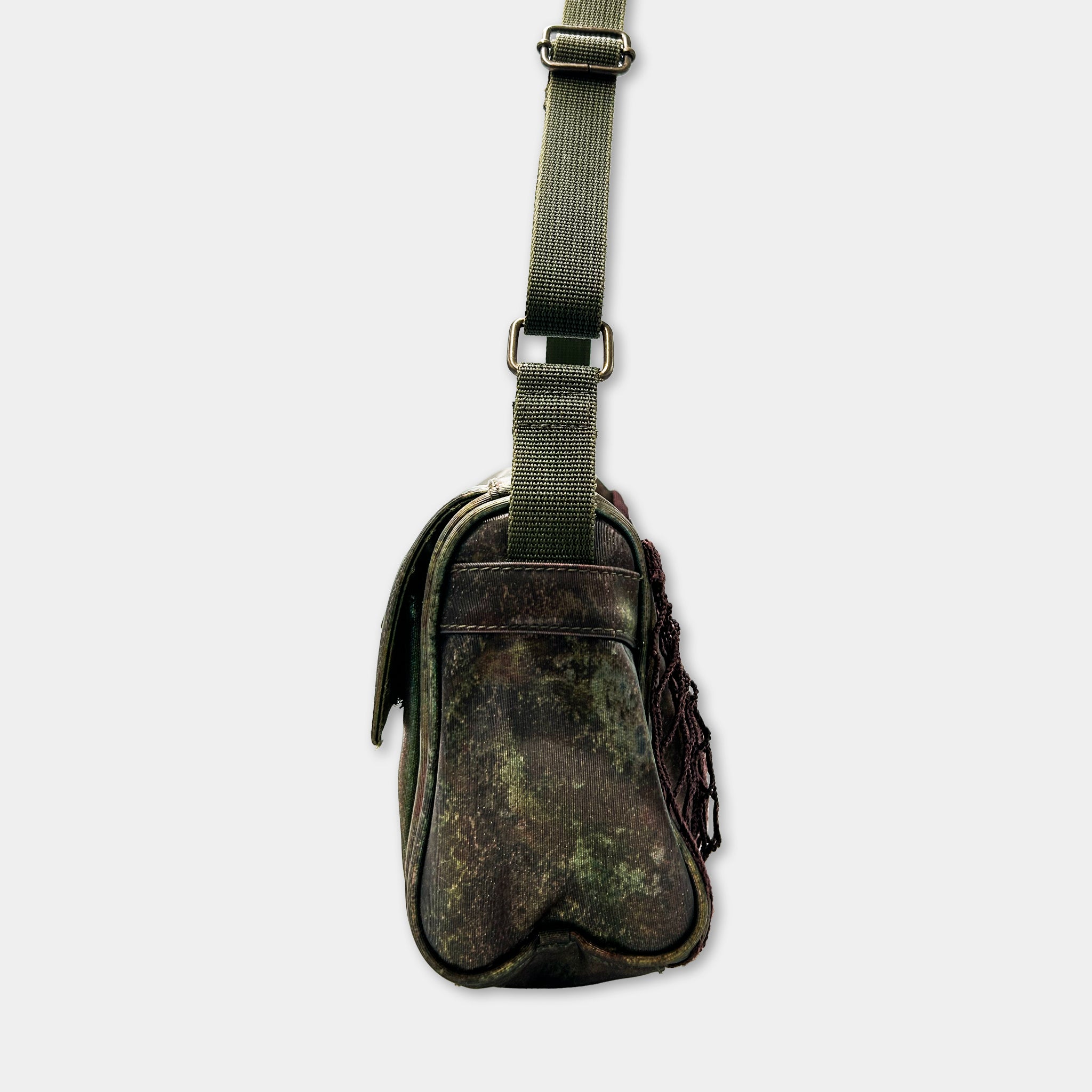A camouflage-patterned bag with a green strap and buckle, hanging against a white background.