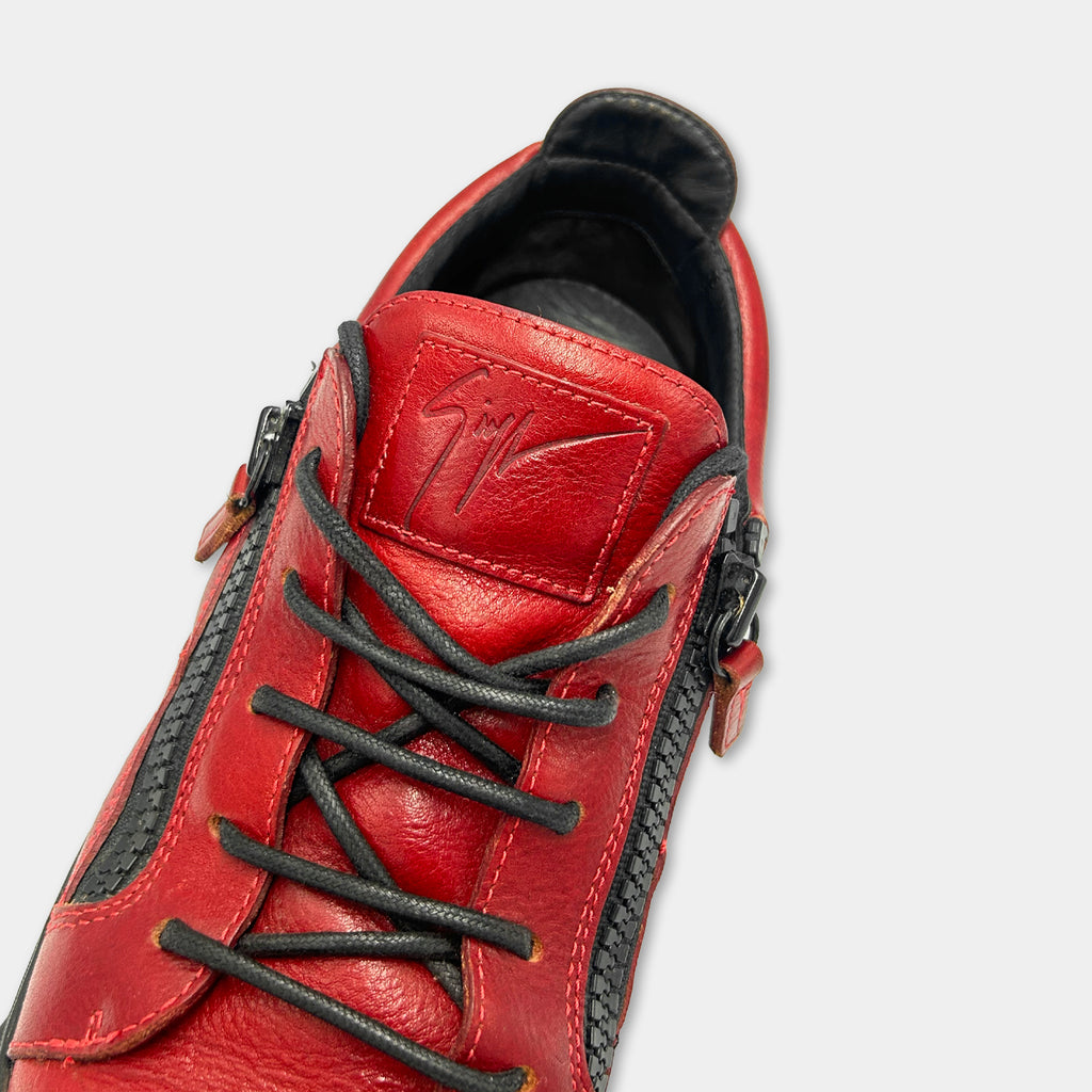 A close-up view of a red leather shoe with black zippers and laces.