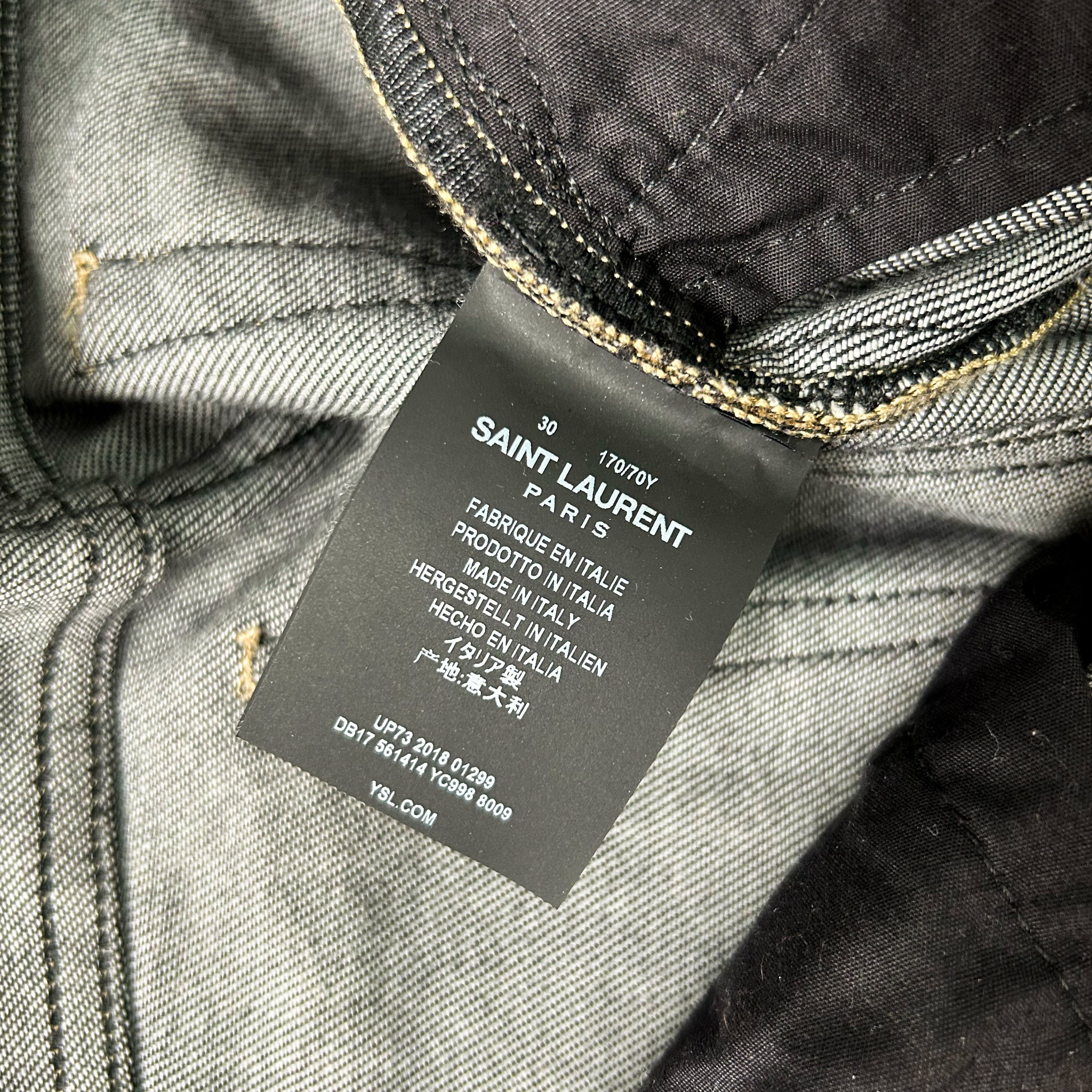 a close-up view of a black label on a pair of gray jeans, with text indicating the brand and material.