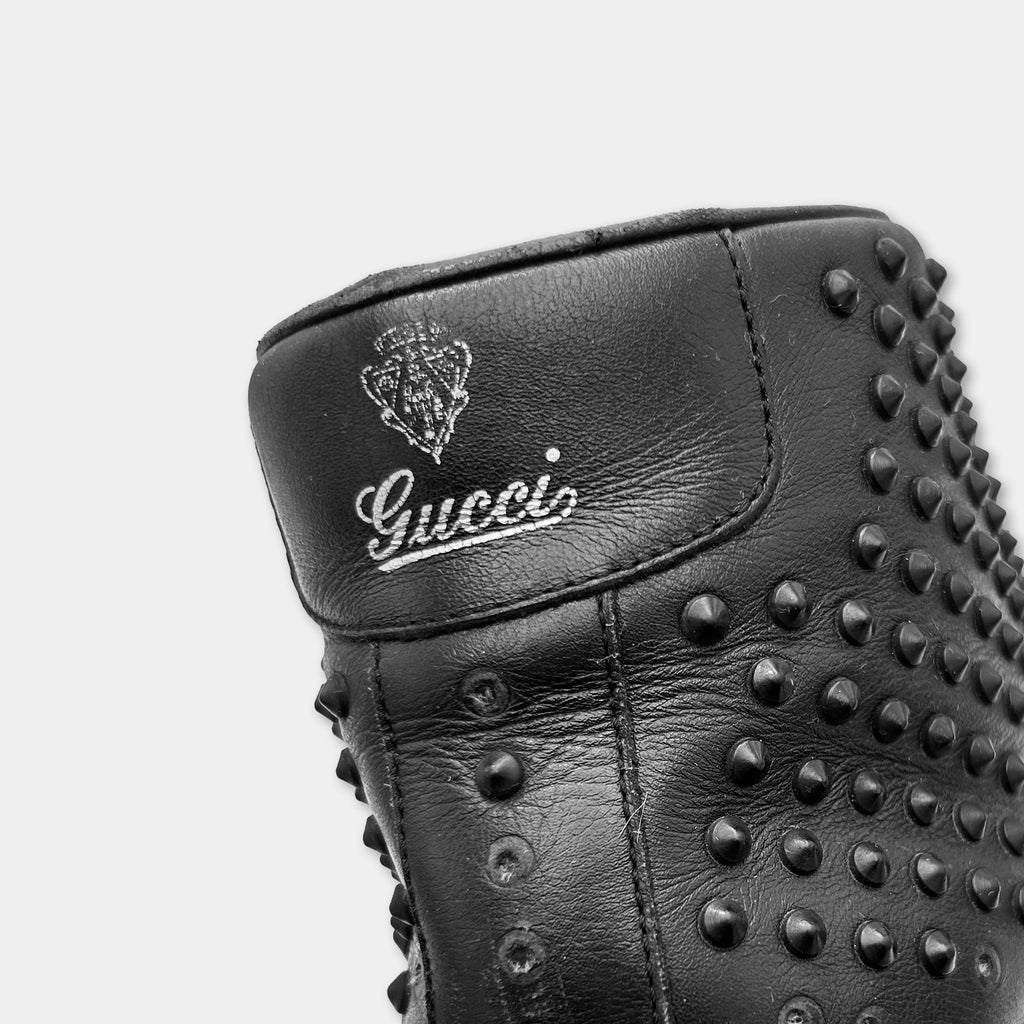 A close-up view of a black leather boot with a textured surface and studded pattern.