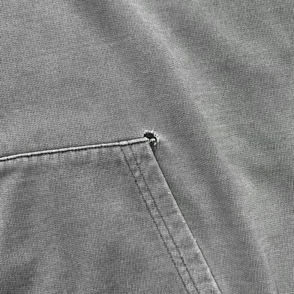 A close-up view of a gray fabric, possibly a piece of clothing, with a small tear or rip in the fabric.