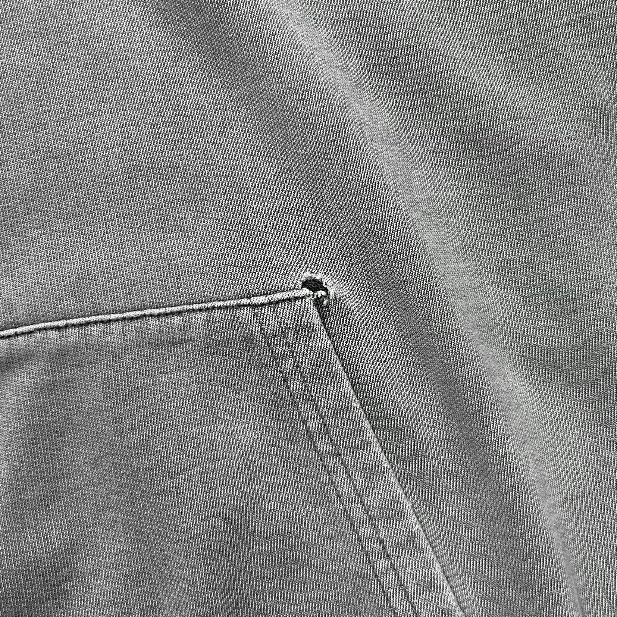 A close-up view of a gray fabric, possibly a piece of clothing, with a small tear or rip in the fabric.