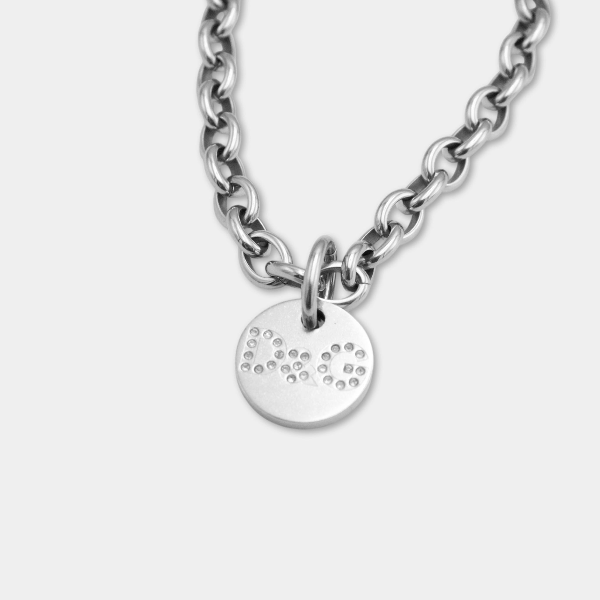 A silver-colored necklace with a circular pendant featuring a pattern of small dots or circles.