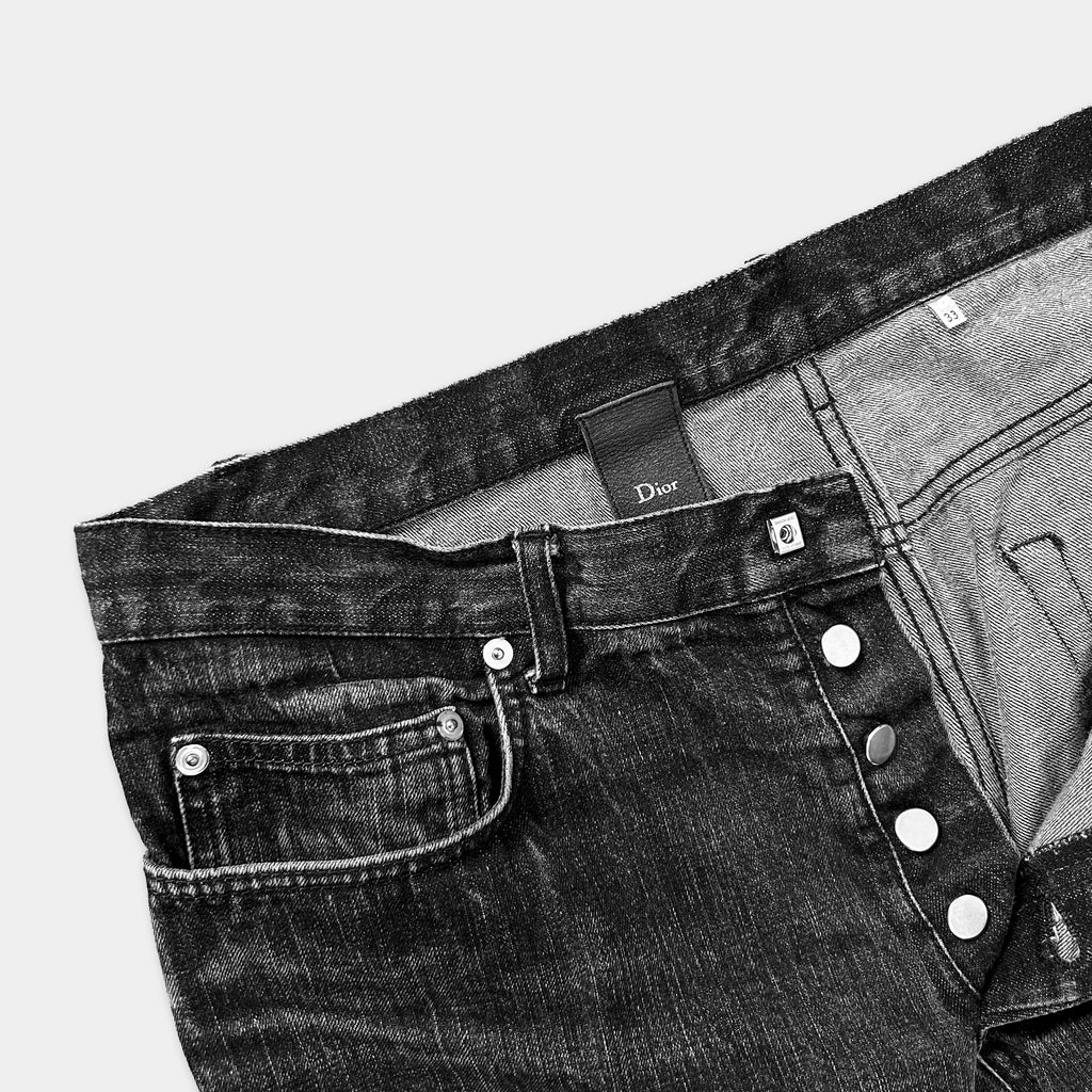 A pair of black denim jeans with a Dior brand tag visible.