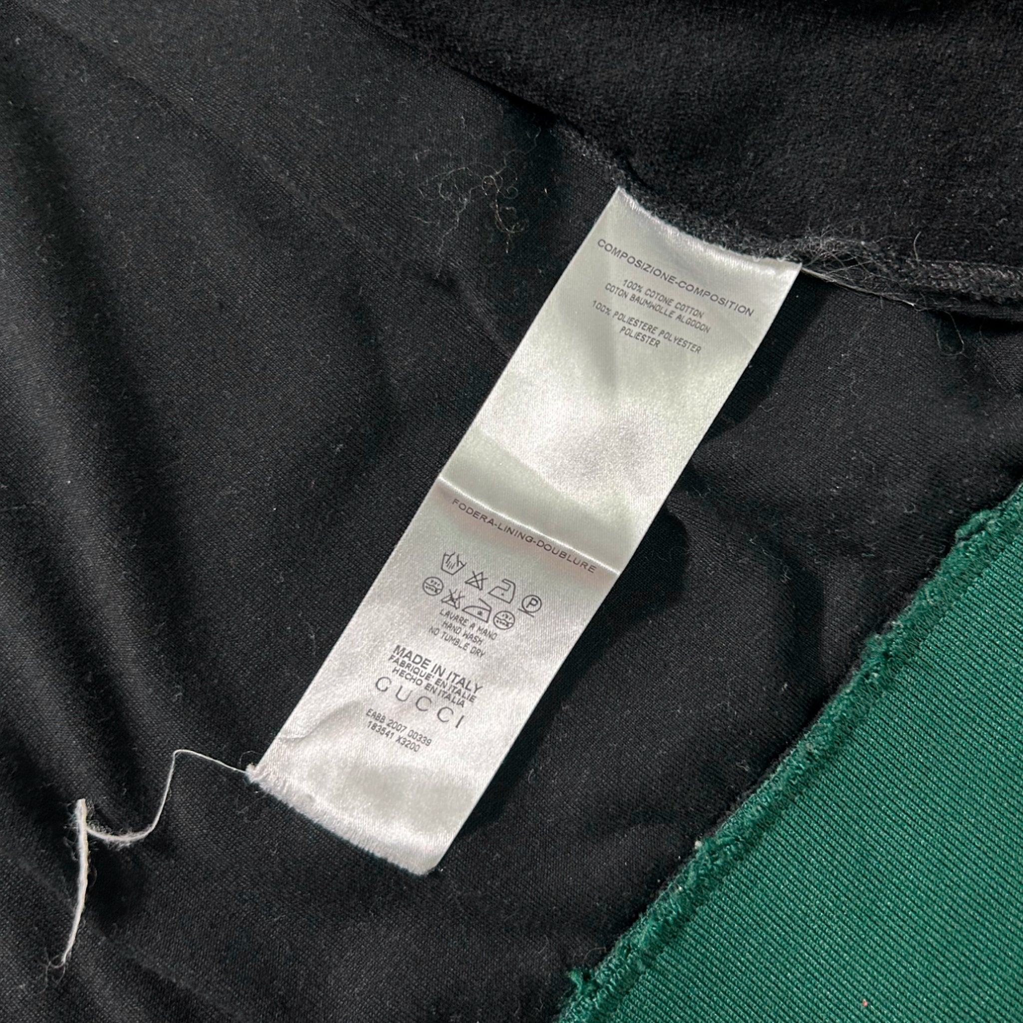a close-up view of a white label attached to a black fabric, with some green fabric visible on the right side.