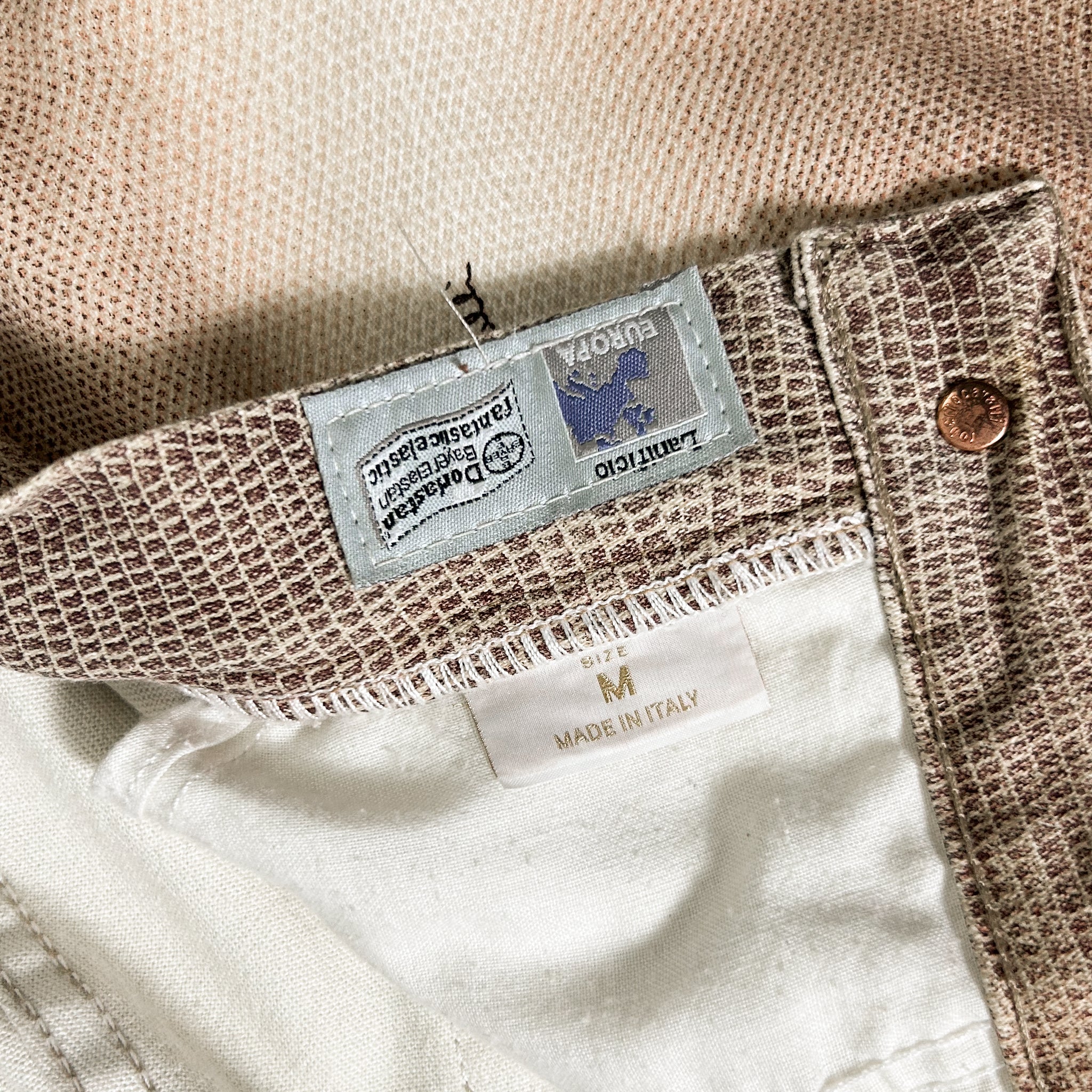 a close-up view of a pair of beige and brown patterned pants, with a label attached to the waistband.