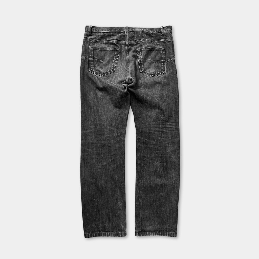 A pair of black jeans with visible signs of wear and tear, including faded and distressed fabric.