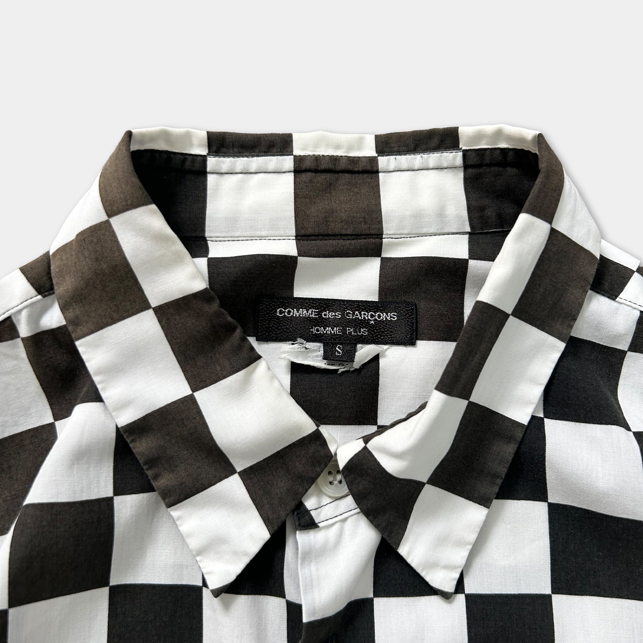 a close-up view of a black and white checkered shirt collar, with a label on the collar that reads "COMMERCES GARONS S".