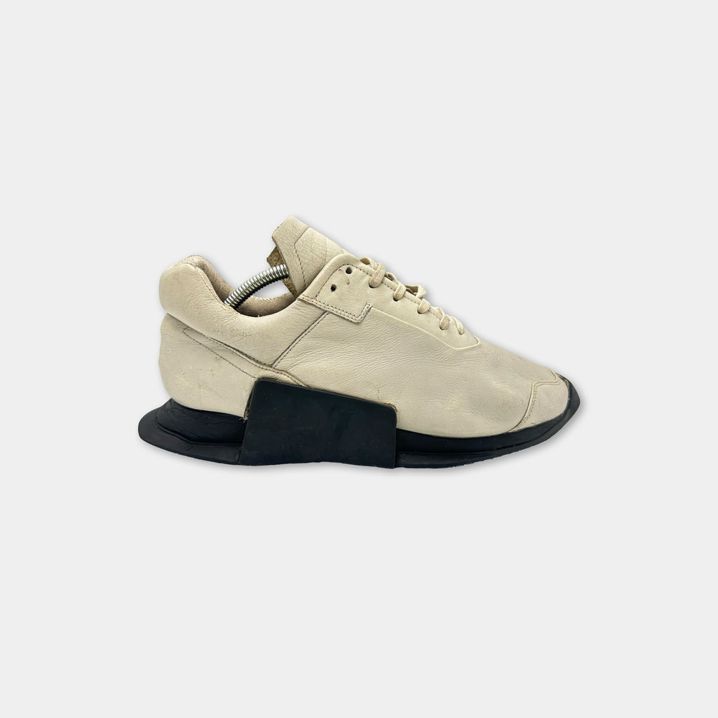 A beige athletic shoe with a black sole and laces is shown against a white background.