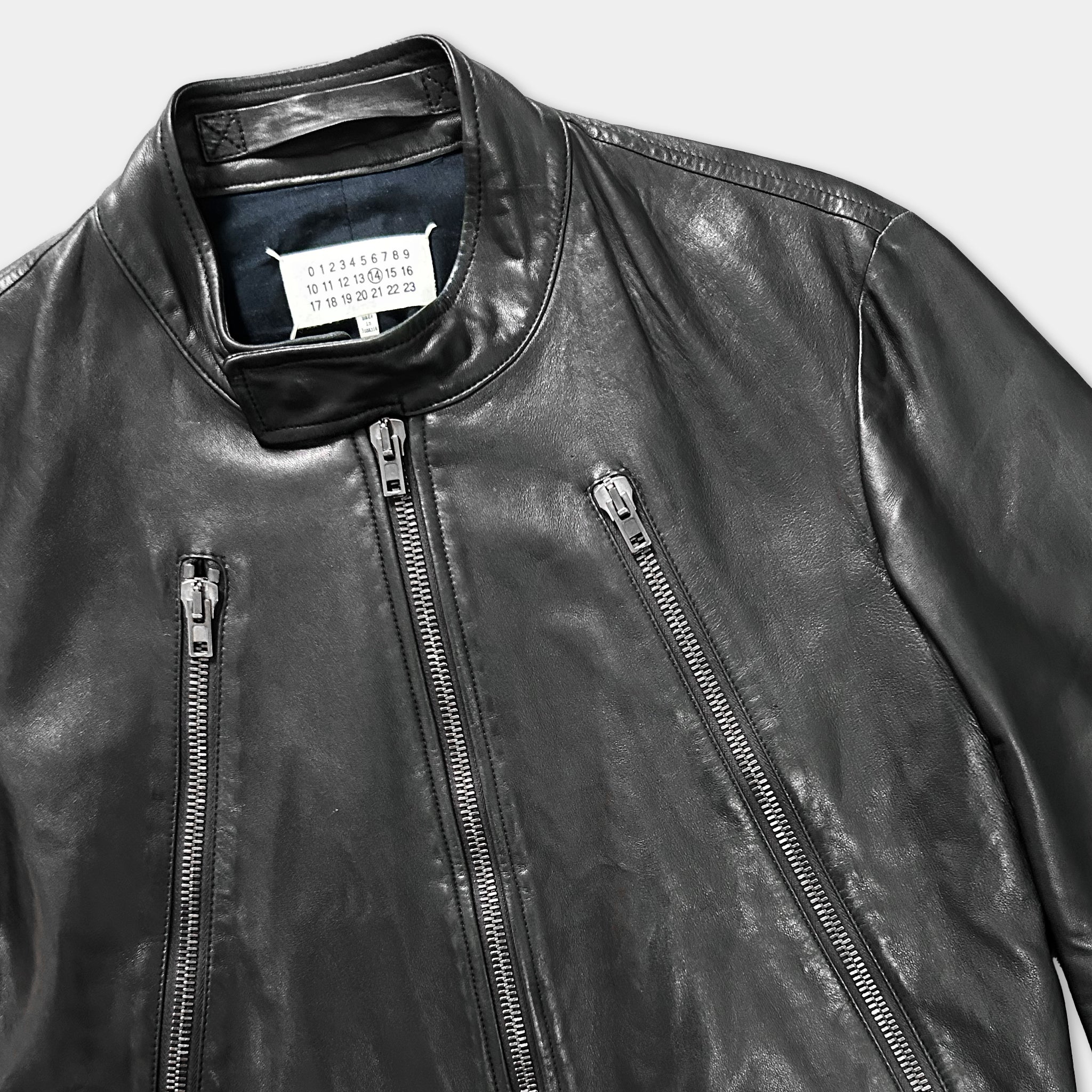 A close-up view of a black leather jacket with multiple zippers and a label on the collar.
