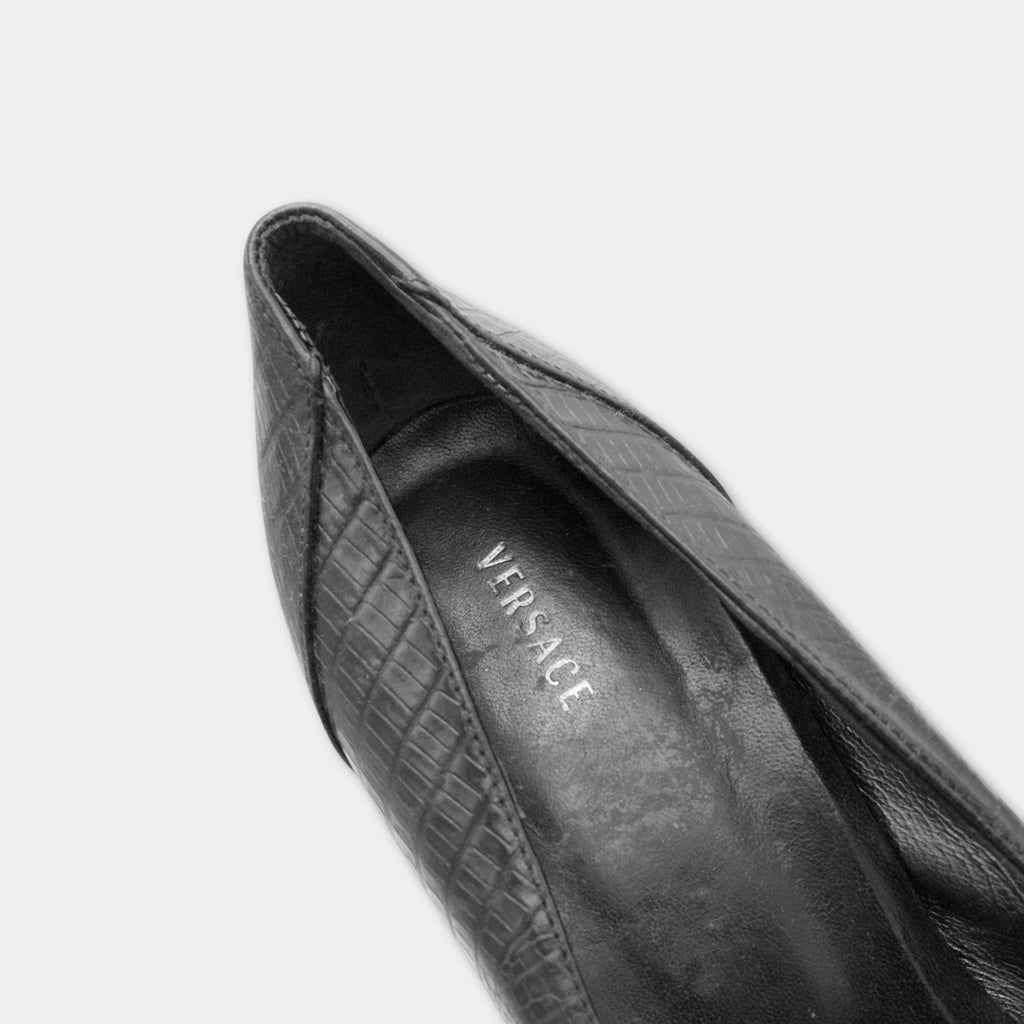 A close-up view of a black leather shoe, specifically a Versace shoe, with the brand name visible on the sole.