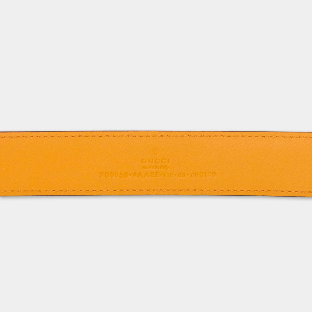 a close-up view of a bright orange leather belt with the Gucci logo and a serial number printed on it.