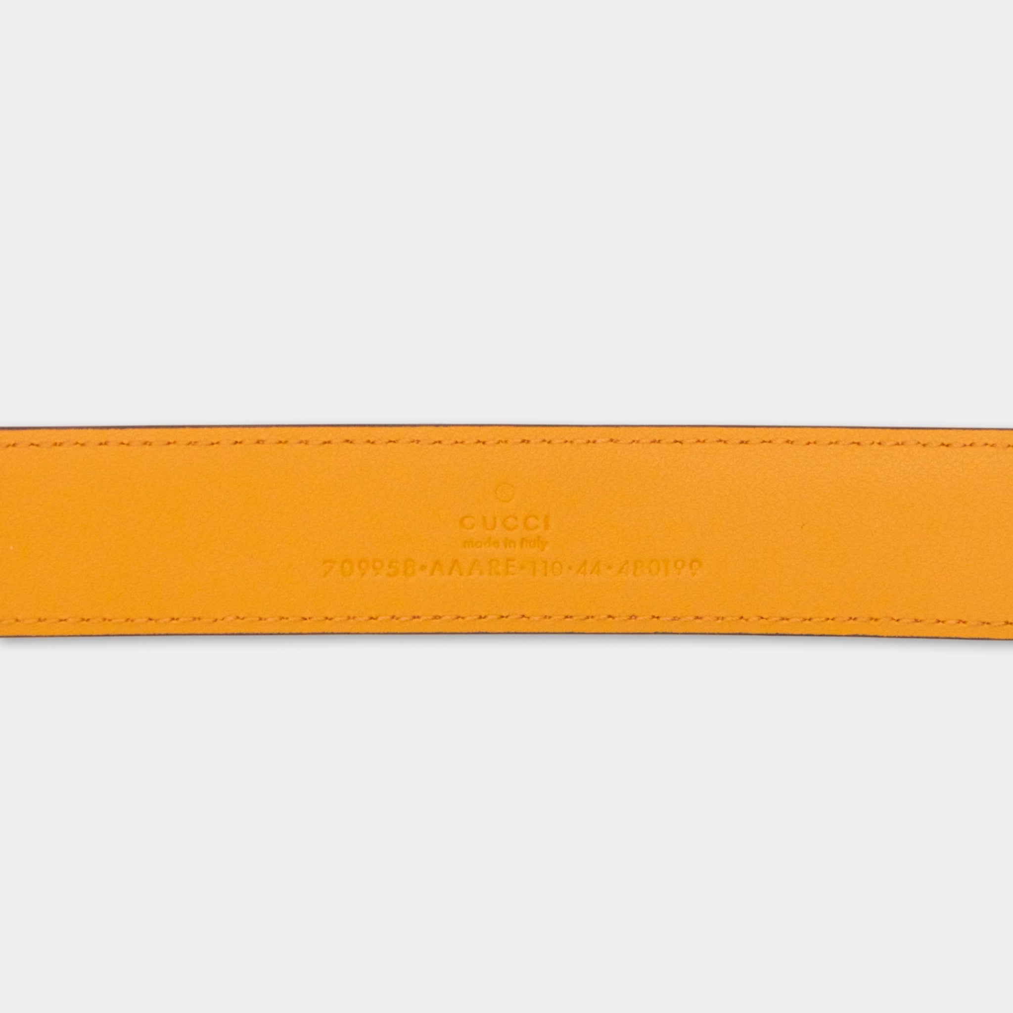 a close-up view of a bright orange leather belt with the Gucci logo and a serial number printed on it.