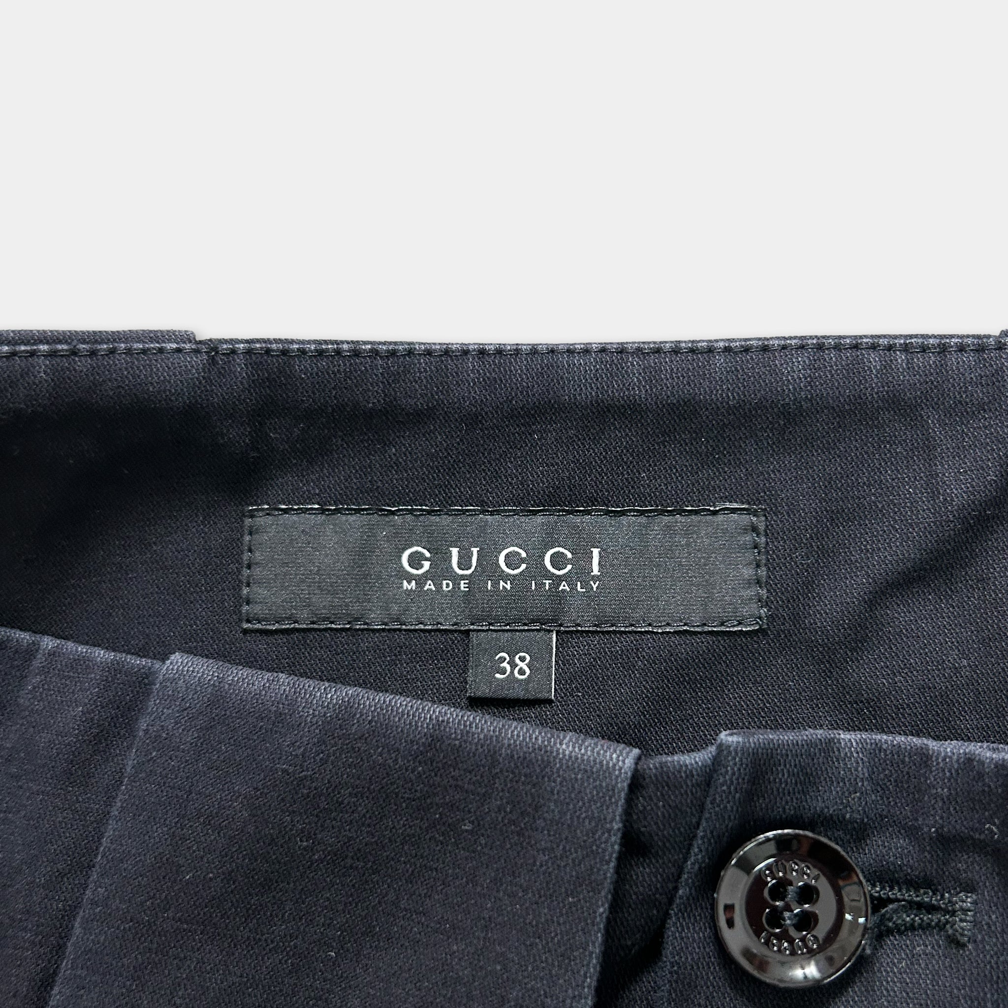 a close-up view of a Gucci clothing label, specifically a pair of dark blue pants. The label displays the Gucci brand name and the text "MADE IN ITALY".