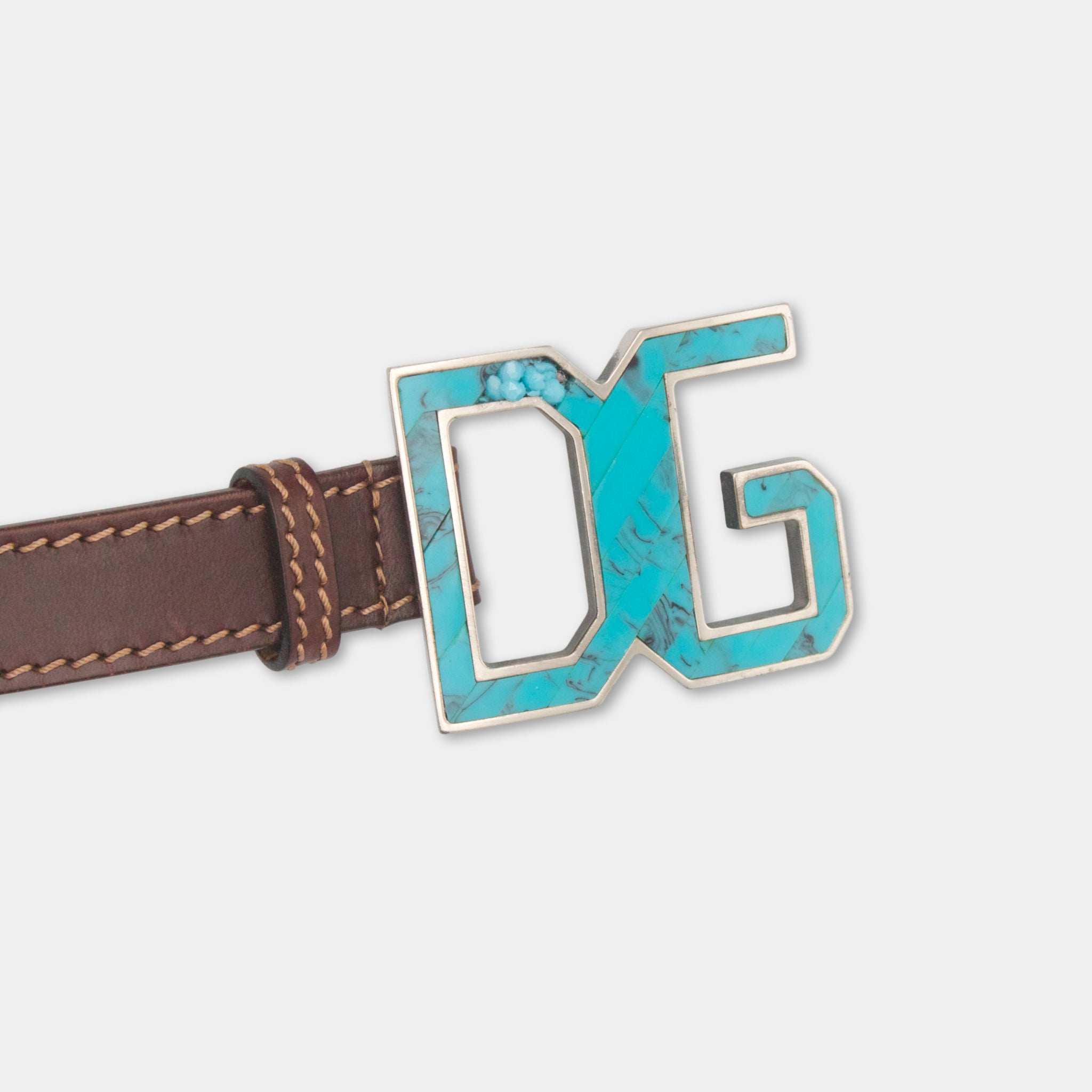 A close-up image of a brown leather belt with a turquoise-colored metal buckle featuring the letters 'DG' on it.