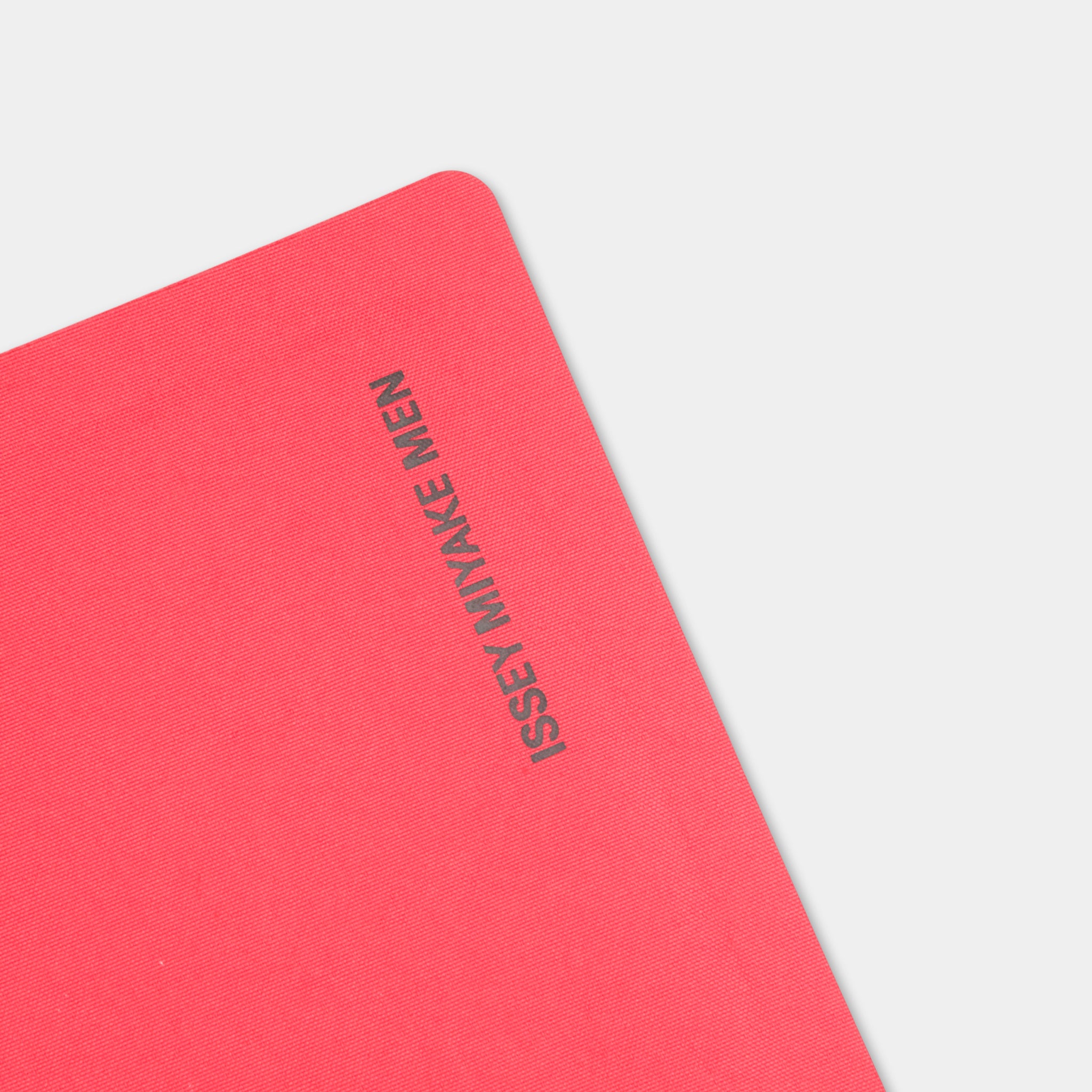 A close-up image of a red notebook with the text "Isey Mijake Men" printed on it.