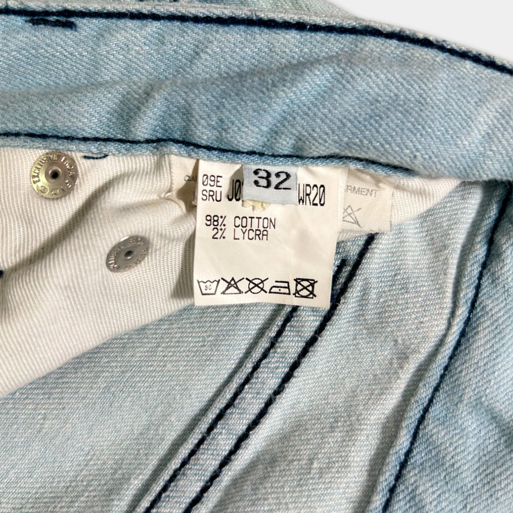a close-up view of a denim fabric, possibly a pair of jeans, with a label attached to it. The label appears to contain information about the fabric, such as the brand, the type of denim, and the care instructions.