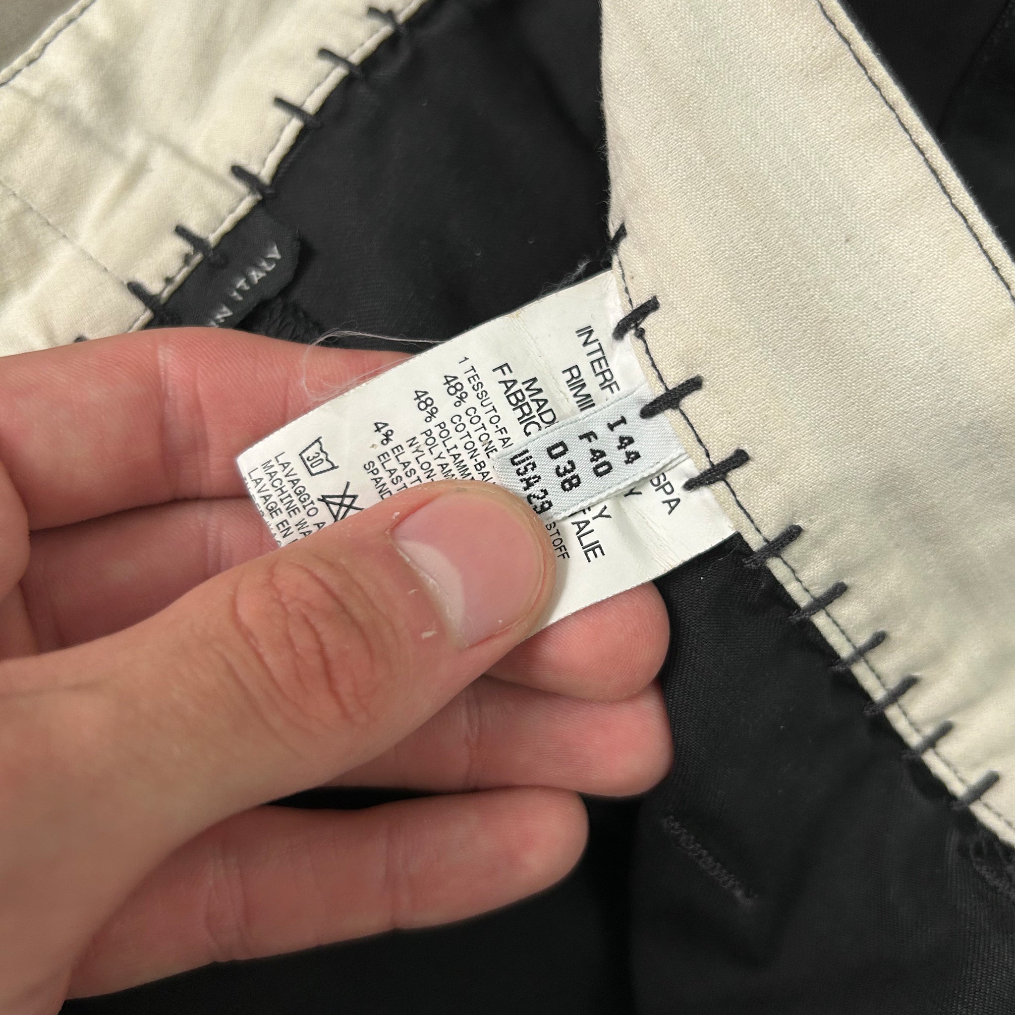 A person's hand holding a label with text and numbers, possibly from a garment or product.