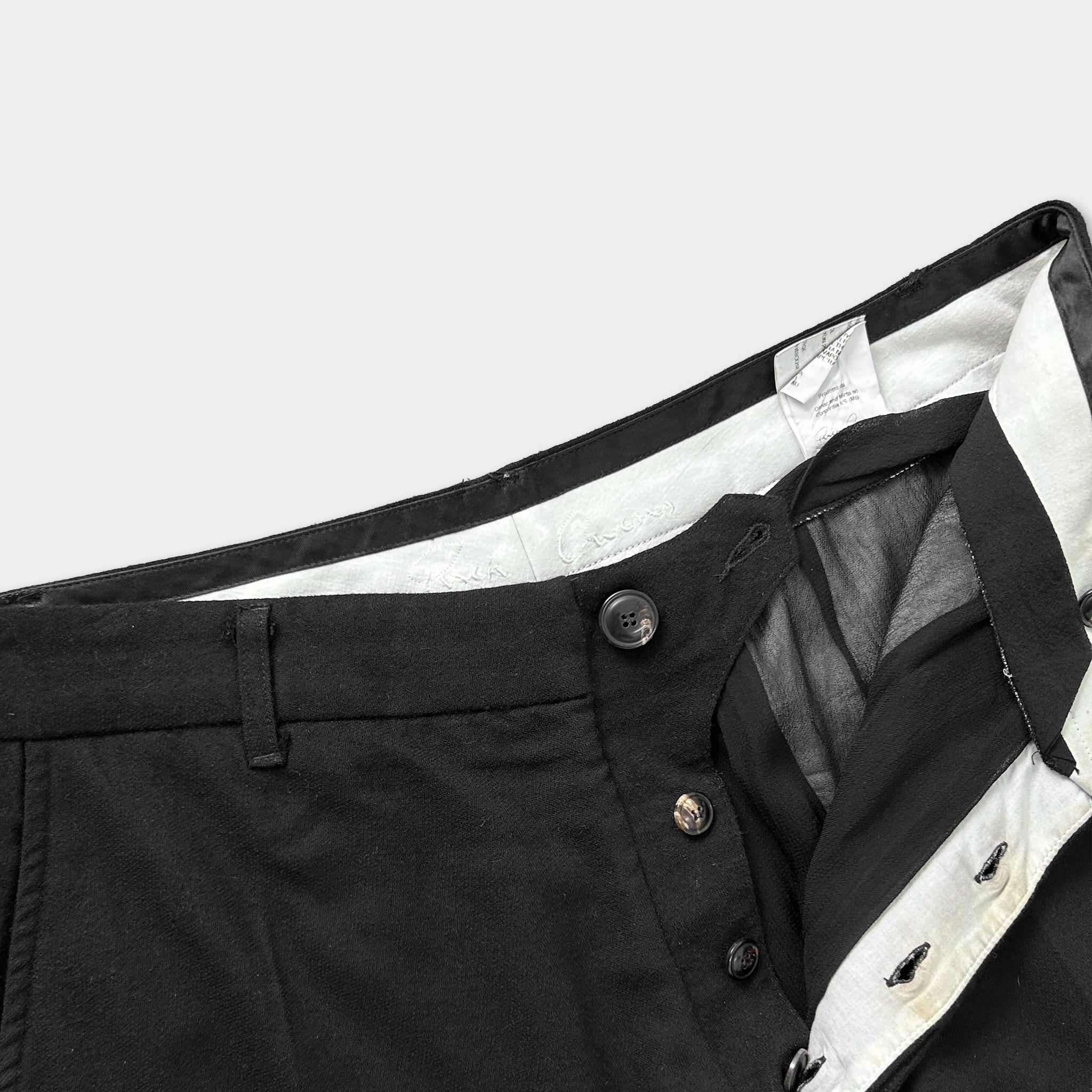 A close-up view of a pair of black trousers with a white label attached to the waistband.