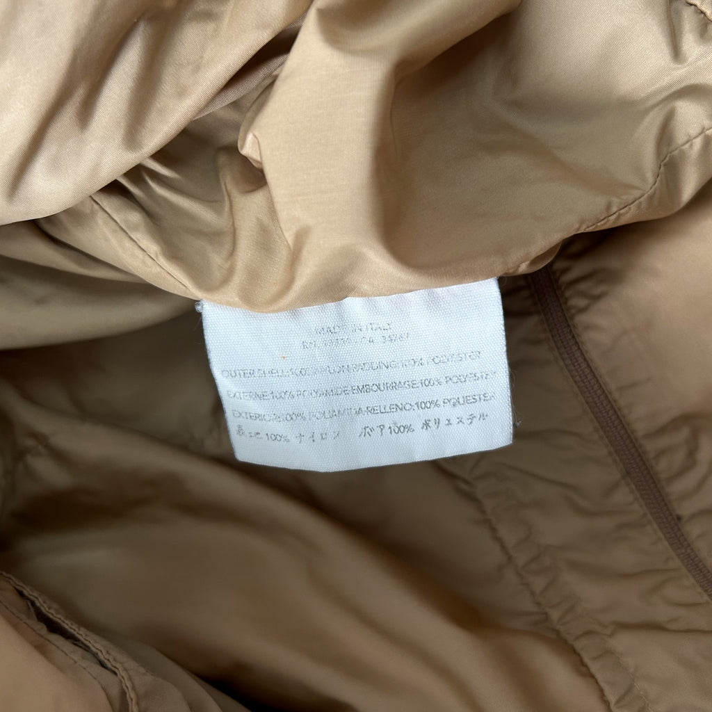 a close-up view of a beige fabric, possibly a jacket or sweater, with a white label attached to it. The label contains text in Italian, which appears to be a description or information about the fabric.