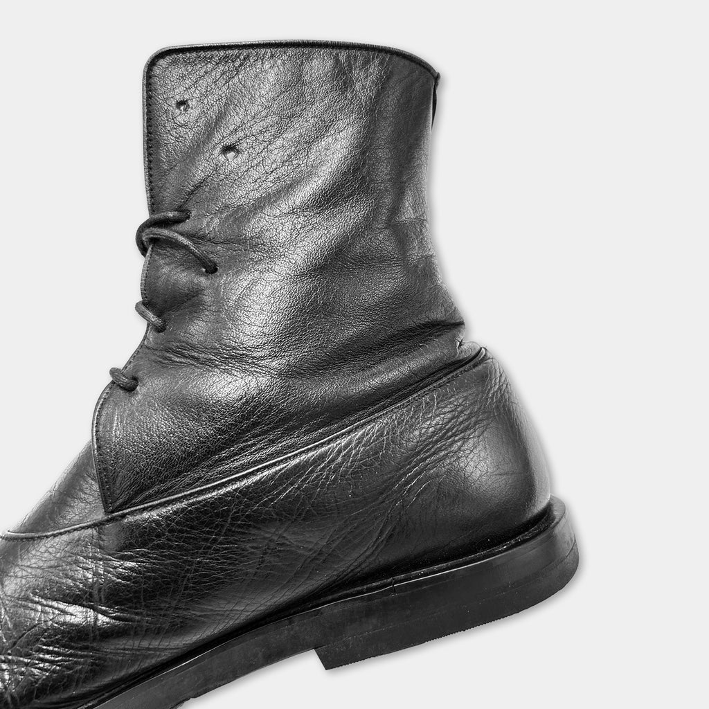 A close-up black and white image of a leather boot with a lace-up closure.