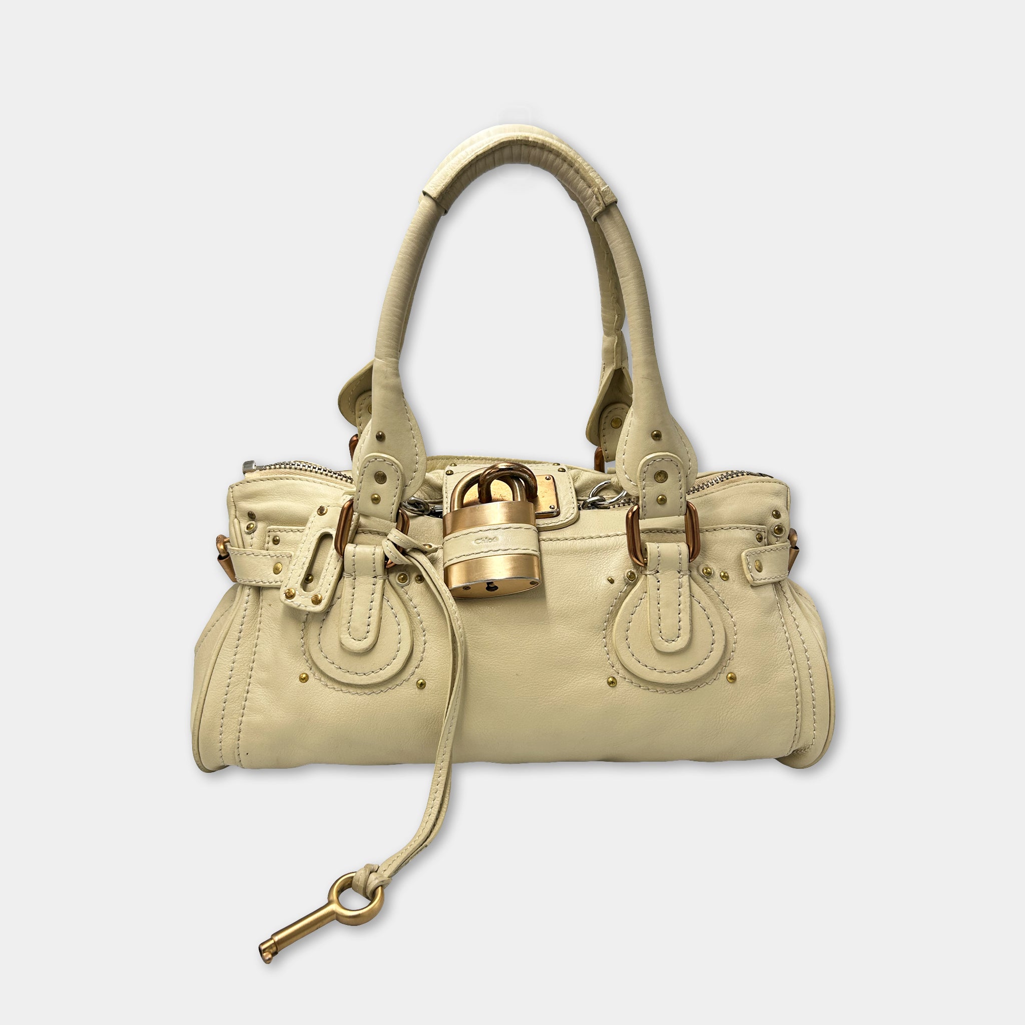 A tan leather handbag with a gold lock and key attached, and a keychain attached to the handle.