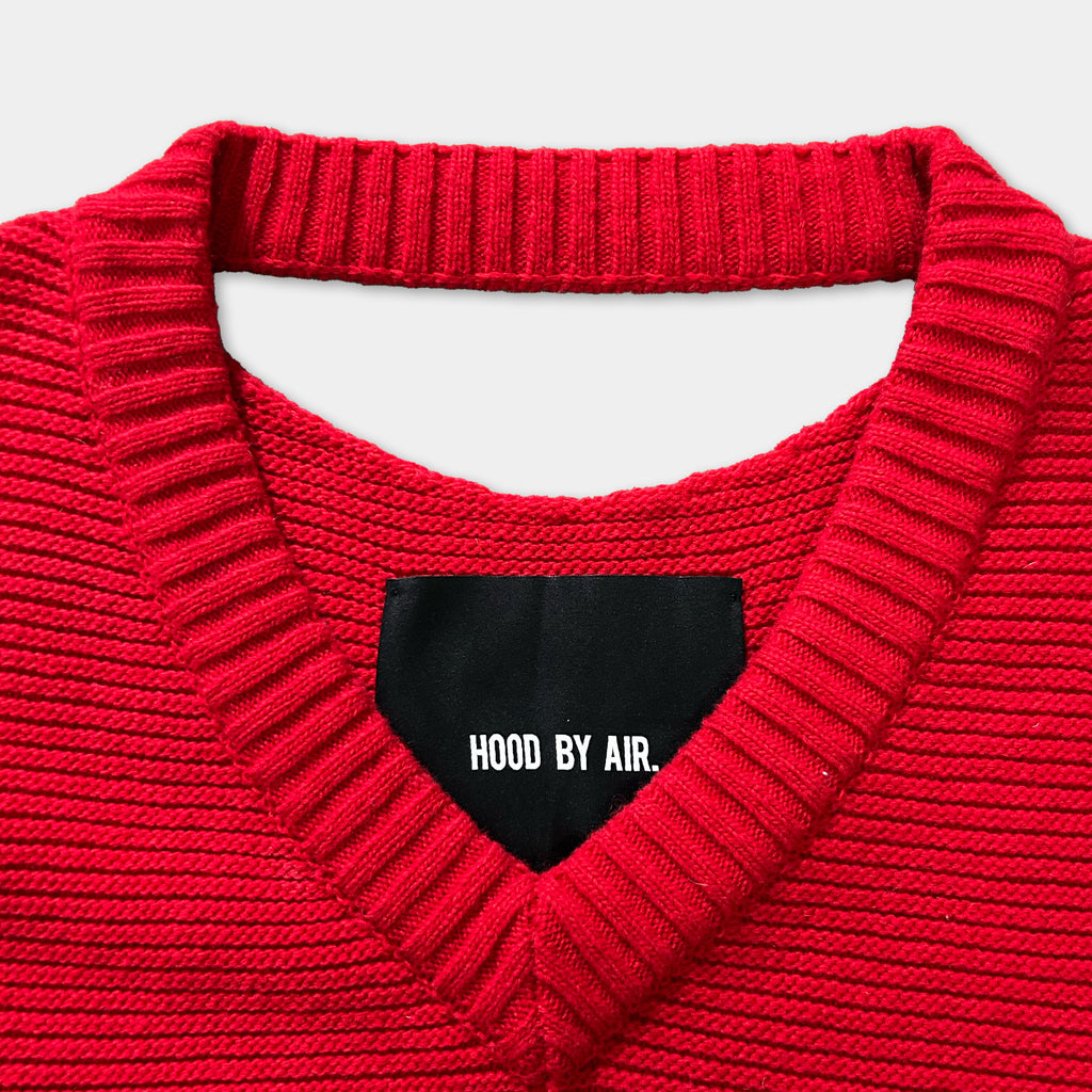 A close-up view of a red knitted sweater with a black label on the collar.