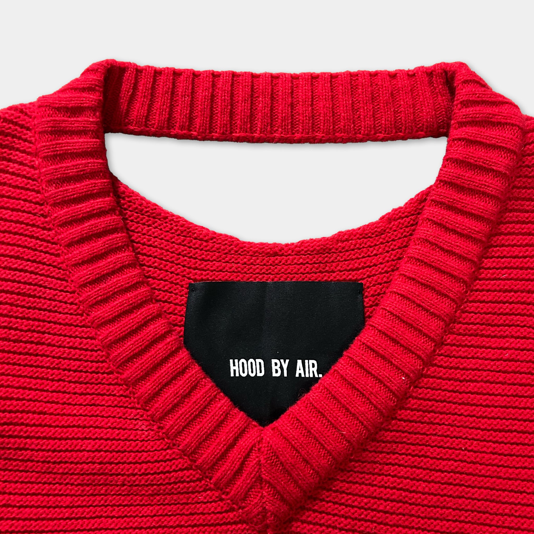A close-up view of a red knitted sweater with a black label on the collar.