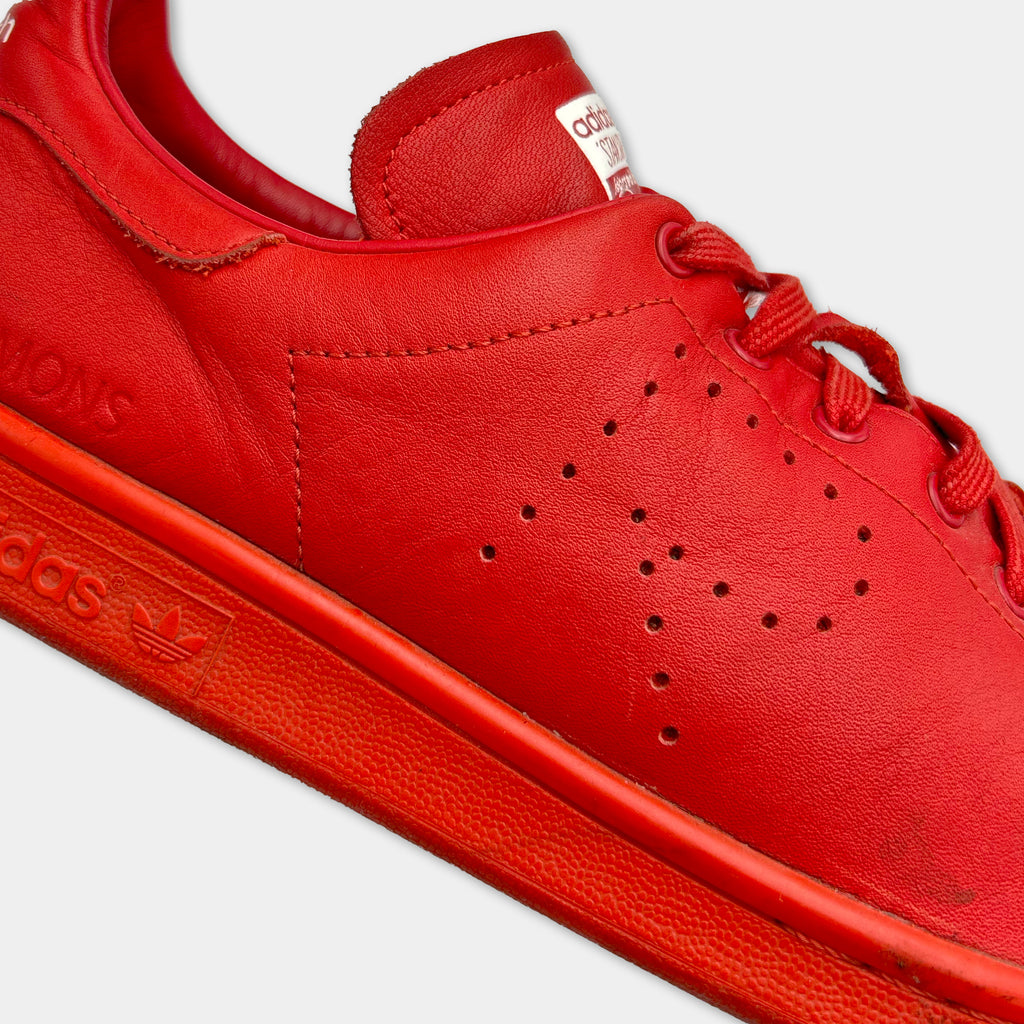 A close-up of a bright red Adidas sneaker with a distinctive pattern of holes on the side.