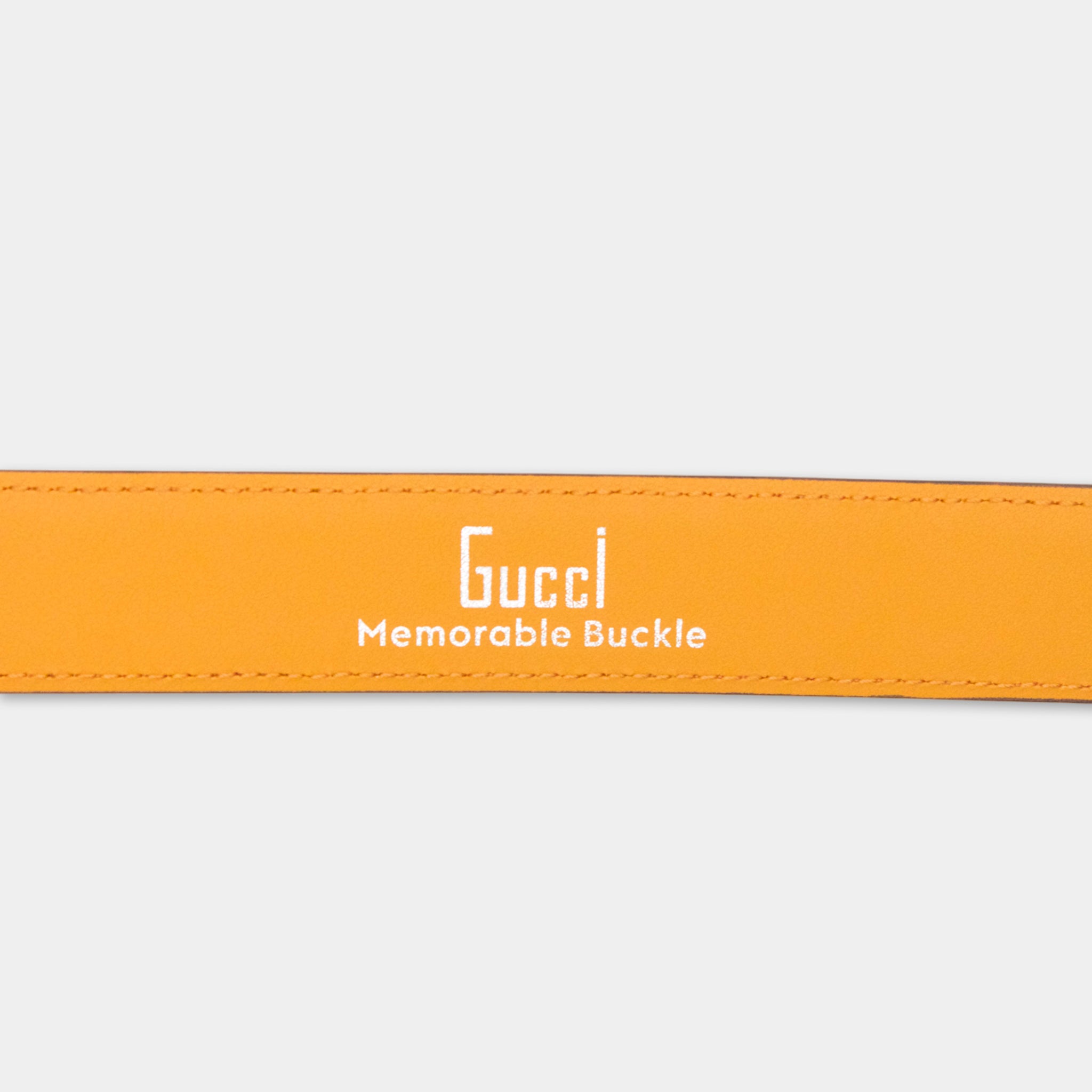 a bright orange Gucci buckle belt with the text "Gucci Memorable Buckle" printed on it.