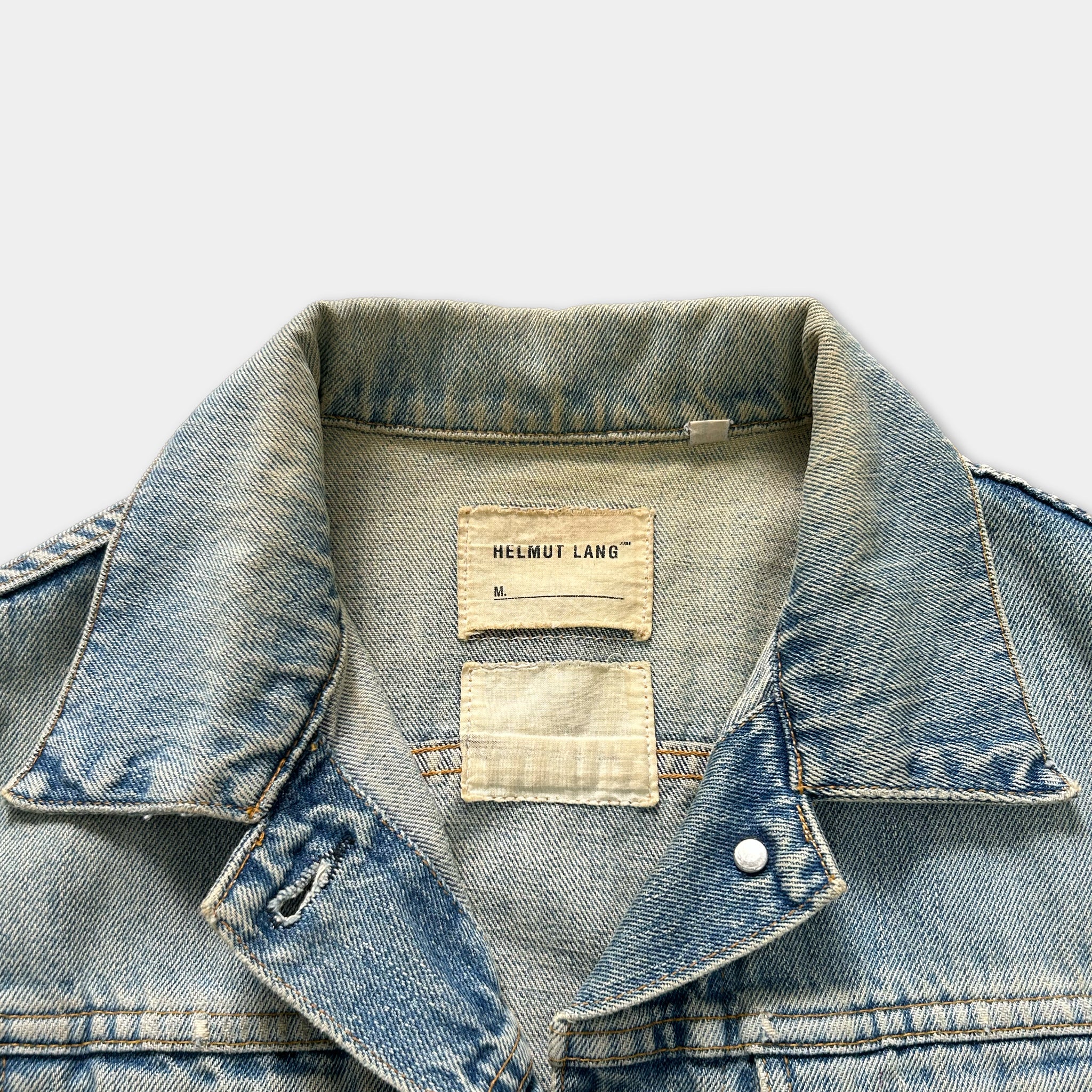 A close-up view of a denim jacket collar and pocket, with a label attached to the collar.