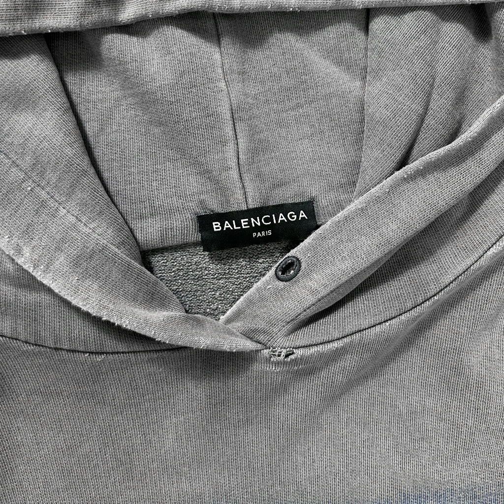 A close-up view of a grey hooded sweatshirt with a label that reads "BALENCIAG" and "FAR".
