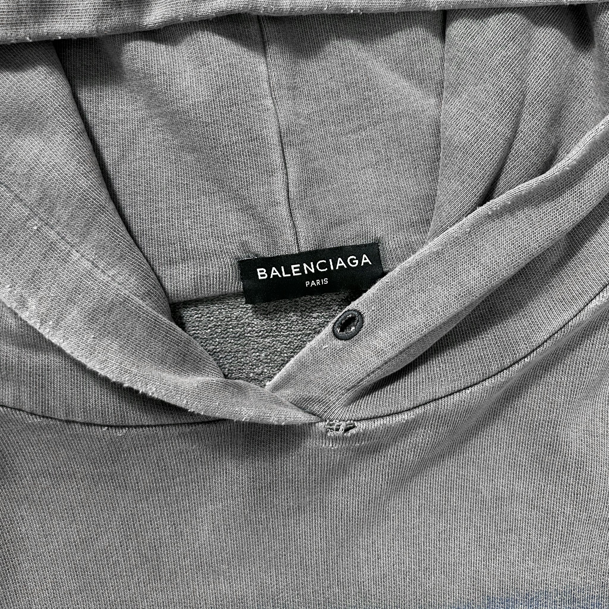 A close-up view of a grey hooded sweatshirt with a label that reads "BALENCIAG" and "FAR".