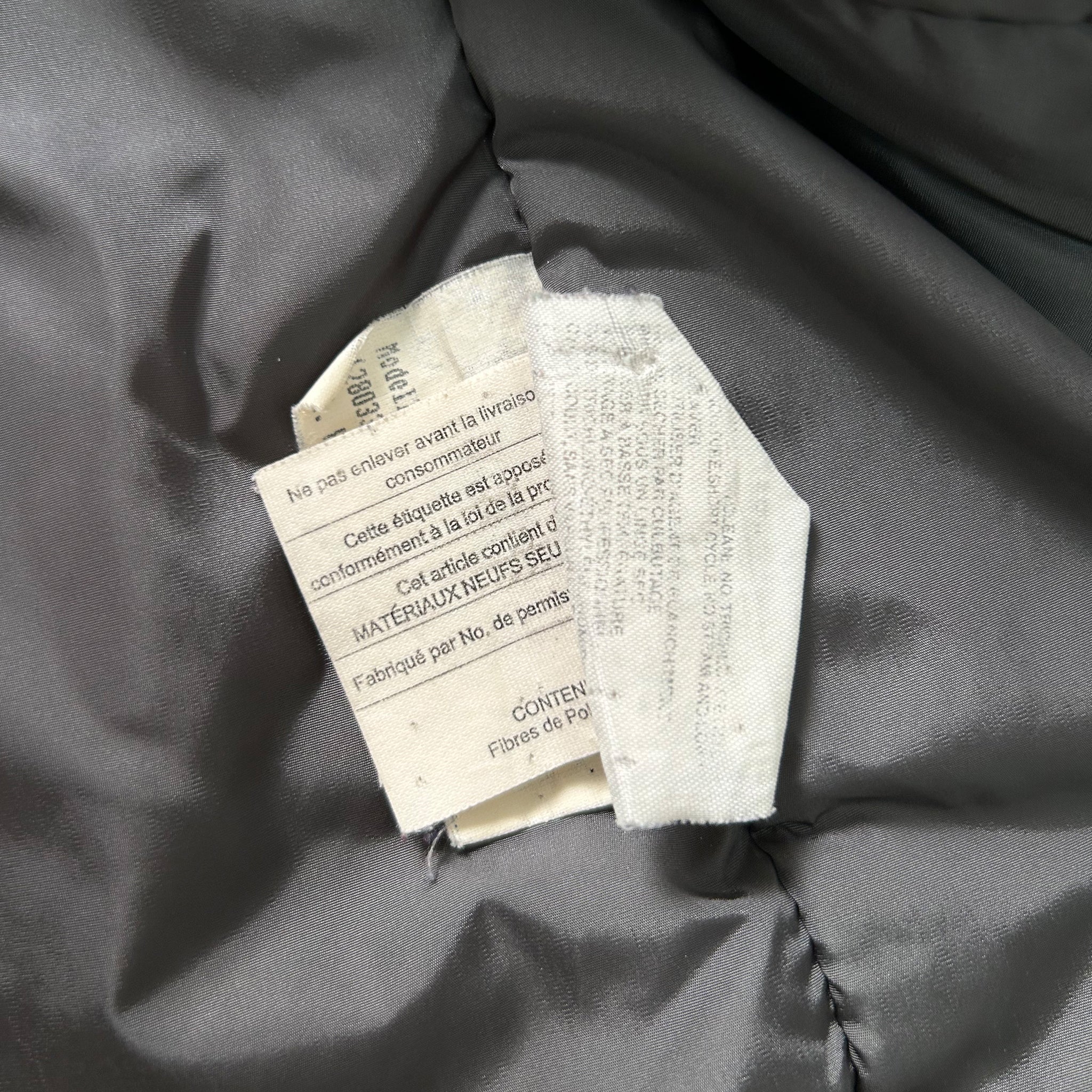 a close-up view of a fabric label attached to a grey fabric, with some text visible on the label.