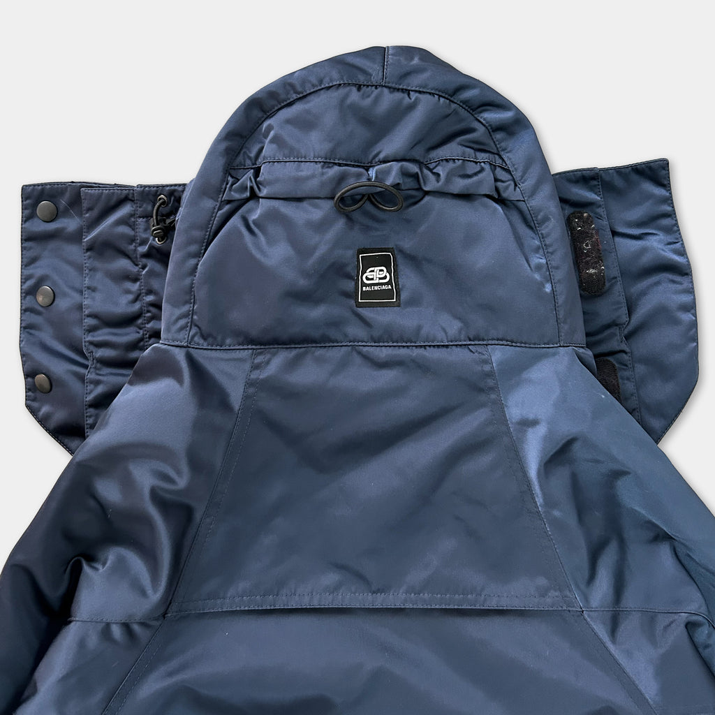 A close-up view of a navy blue jacket with a hood, zipper, and pockets.