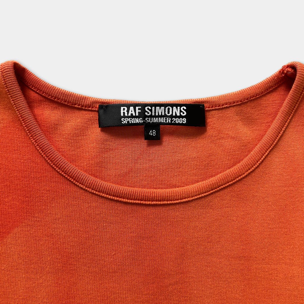a close-up view of a bright orange t-shirt with a label that reads "RAF SIMONS SPRING- SUMMER 2009 48".